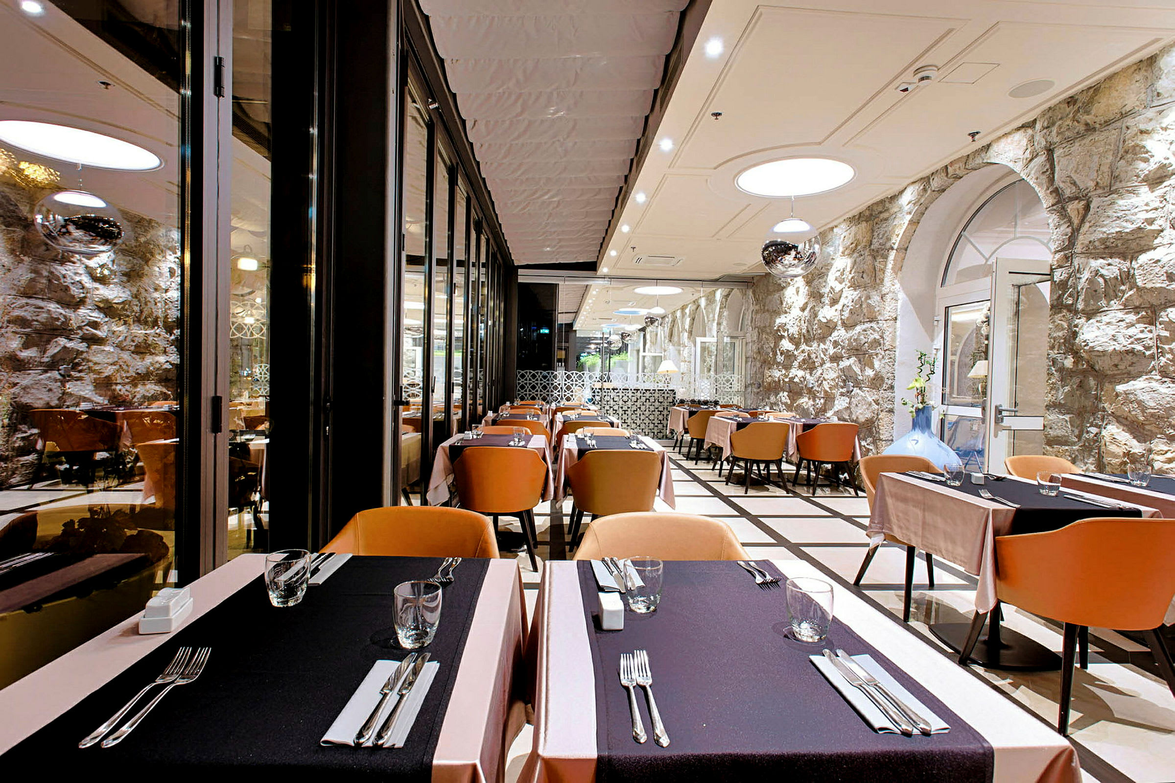 Bild av en elegant restaurang med dukade bord och stolar, stenmur som bakgrund. (AI-genererad text)