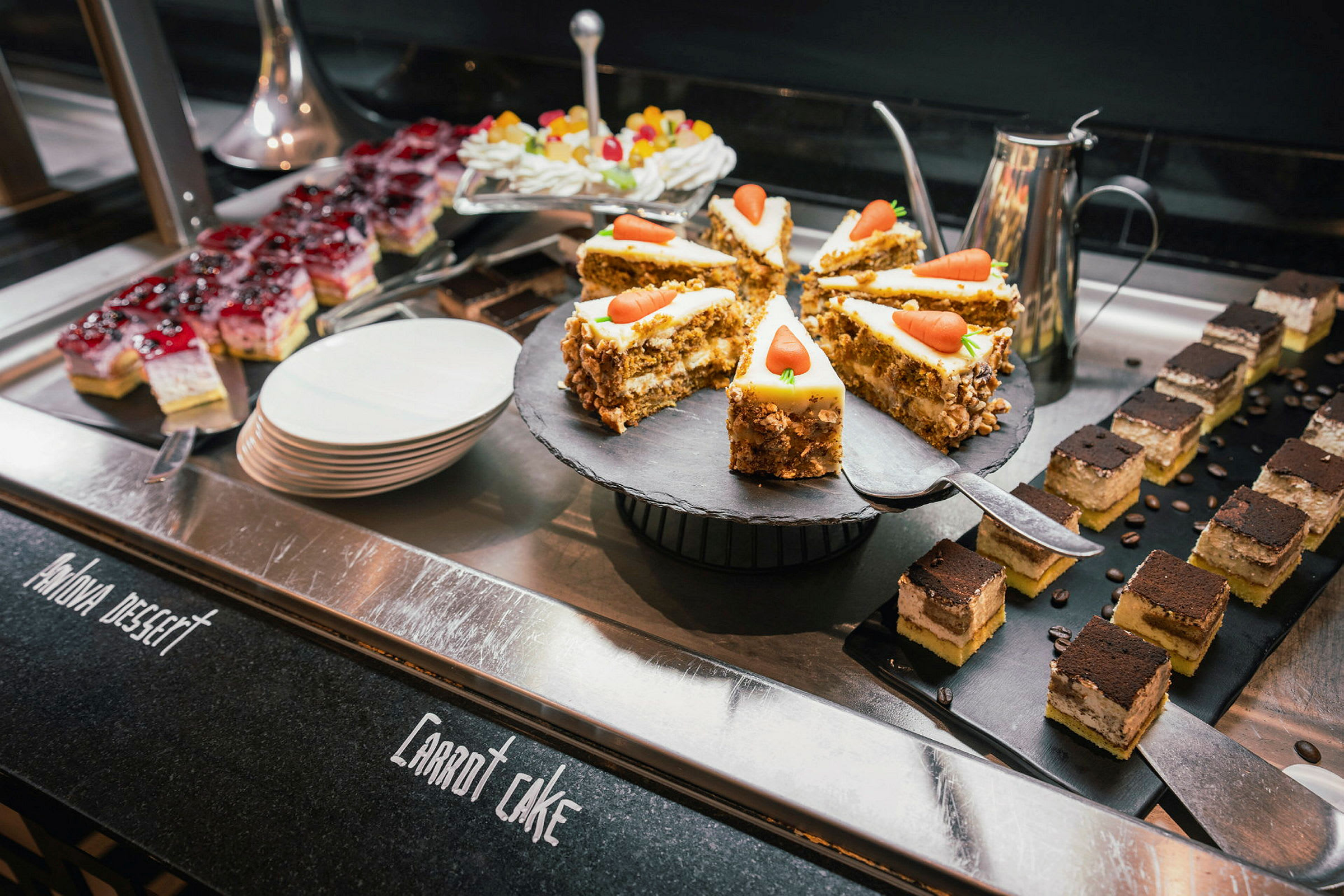 Bilden visar en buffé med olika desserter, inklusive morotskaka, små vanilj- och chokladtårtbitar samt färgglada gelégodisar. (AI-genererad text)