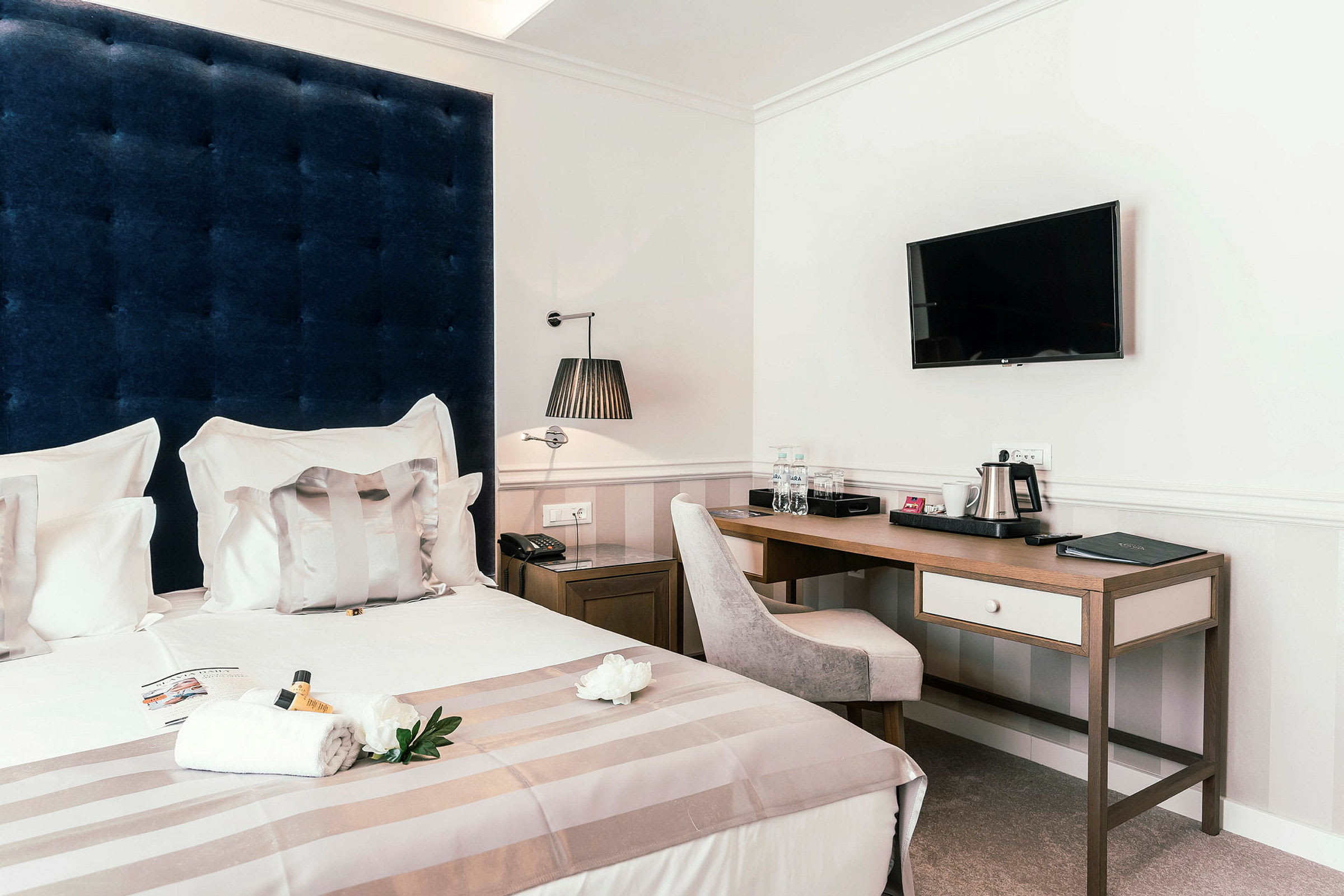 Ett hotellrum med en säng, skrivbord, tv på väggen och bekvämligheter såsom vattenflaskor och kaffekokare. (AI-genererad text)