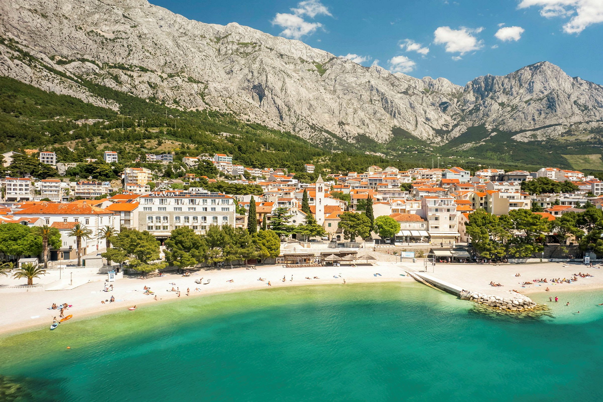 En kuststad vid foten av ett berg med en sandstrand och klart turkost vatten. (AI-genererad text)