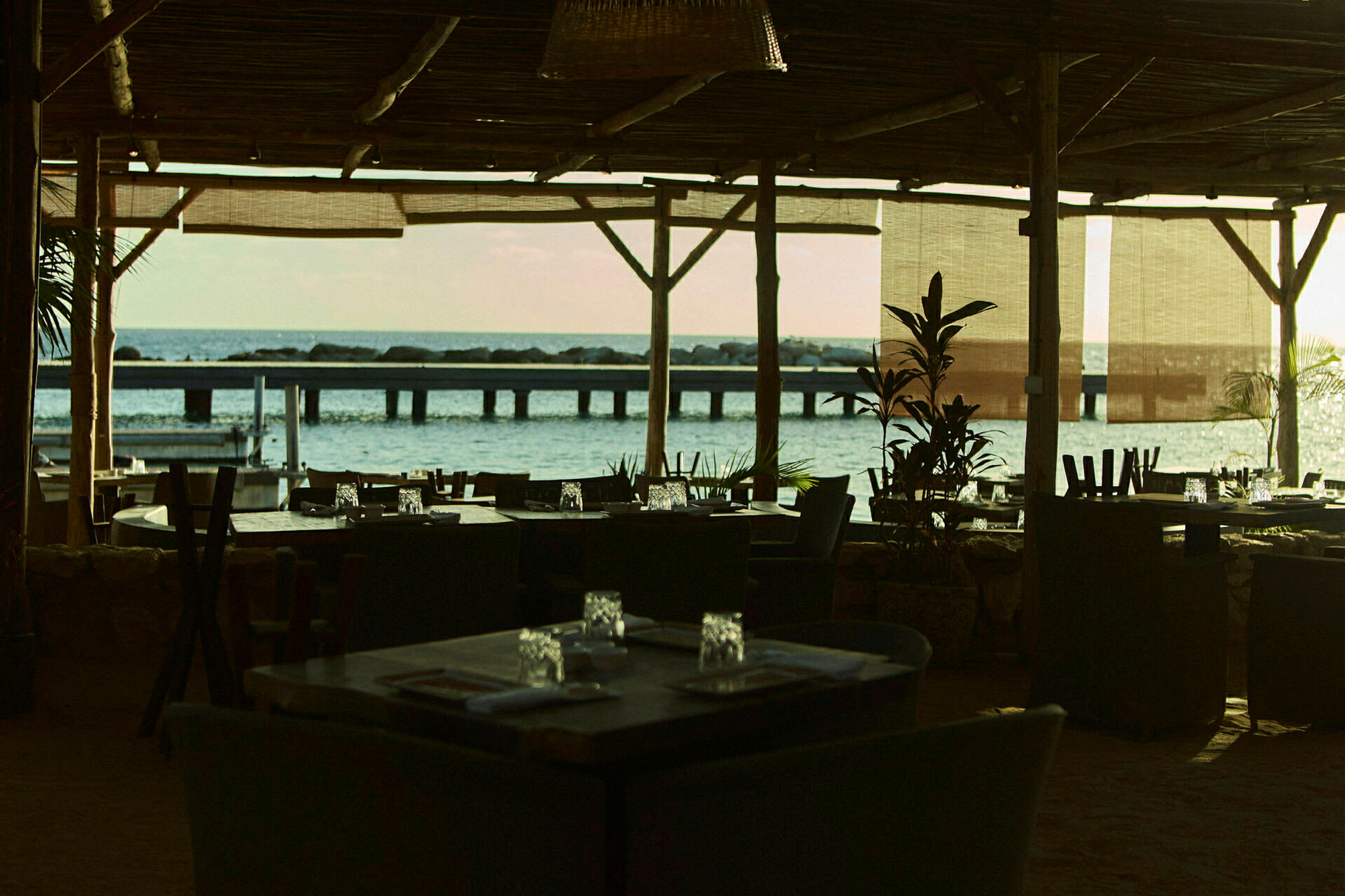 En restaurang med tak och möbler med utsikt över havet och en brygga i bakgrunden. (AI-genererad text)