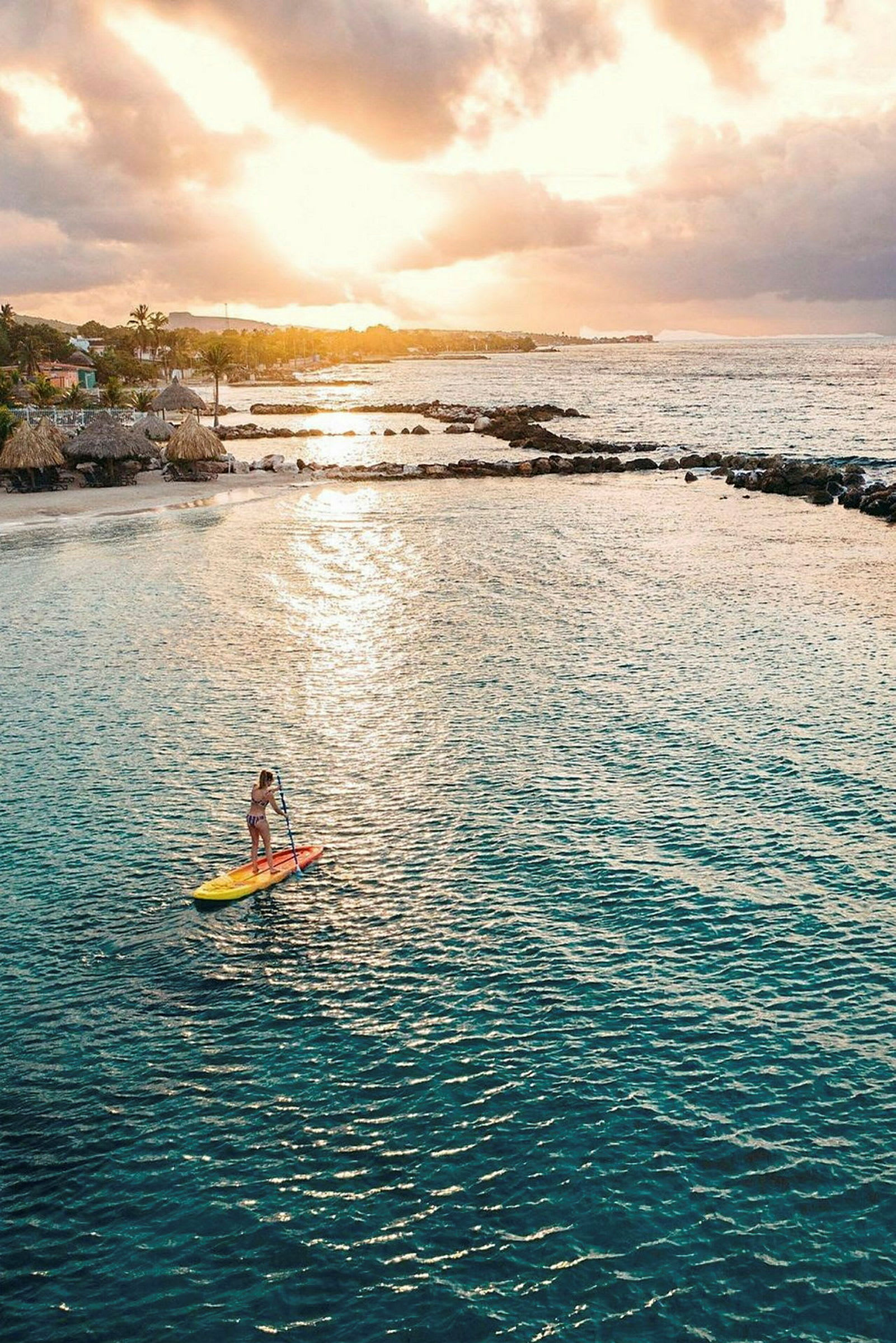 En person som paddlar på en paddleboard i en lugn vik med gyllene solnedgång i bakgrunden. (AI-genererad text)