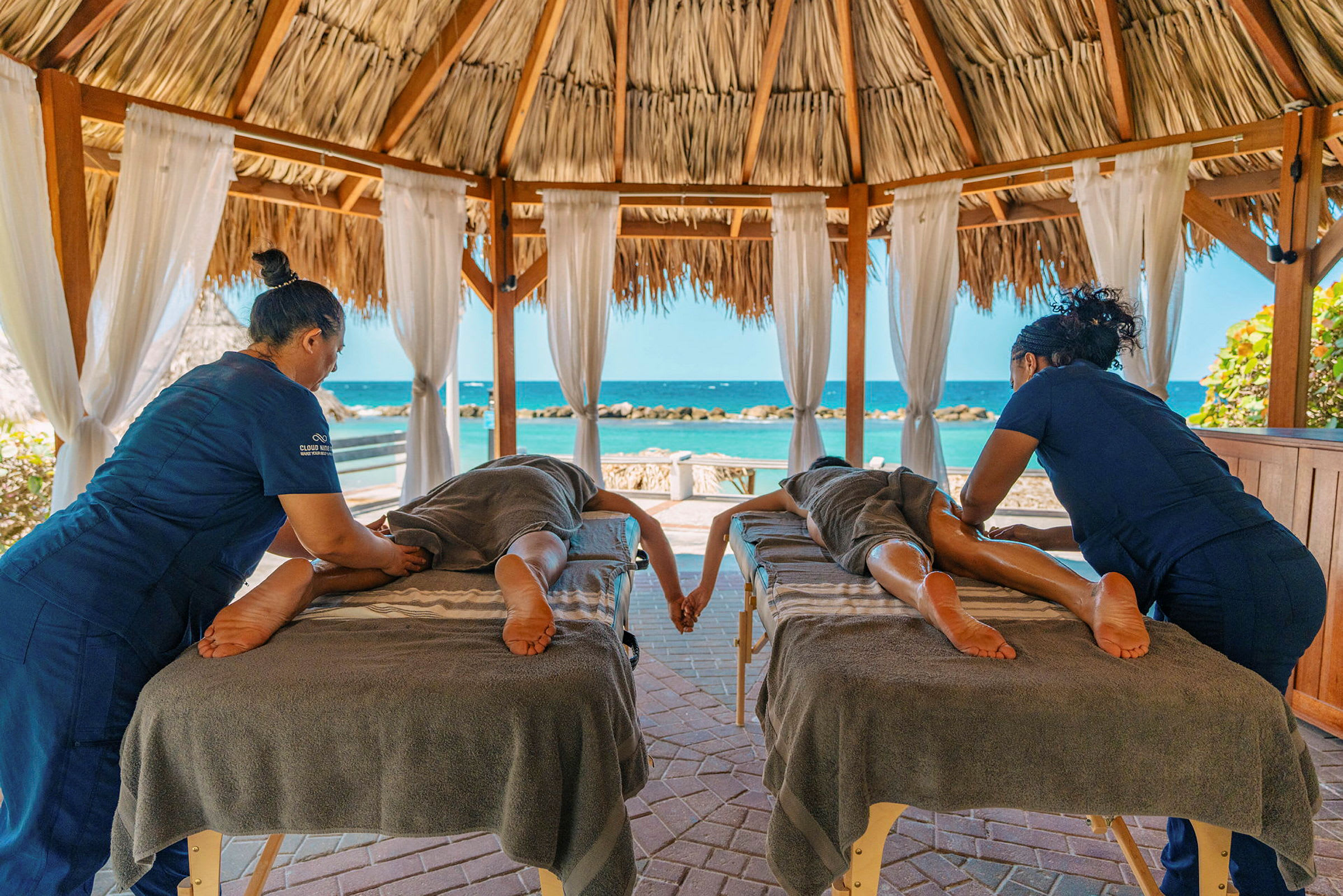 Två personer får massage under ett stråtak med utsikt över havet. (AI-genererad text)