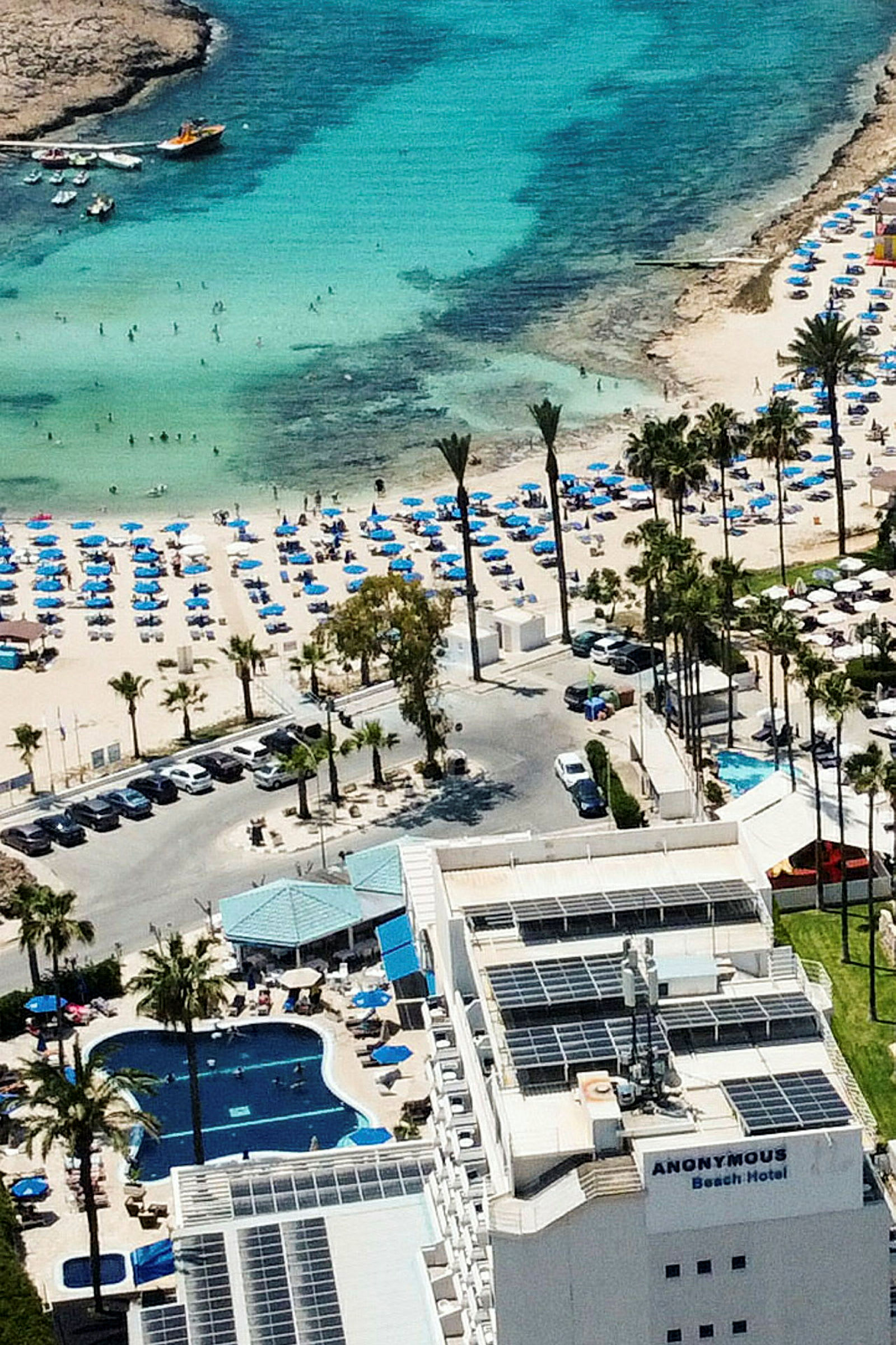 Hotell med pool och närliggande strand fylld med solstolar och parasoller vid ett turkost hav. (AI-genererad text)