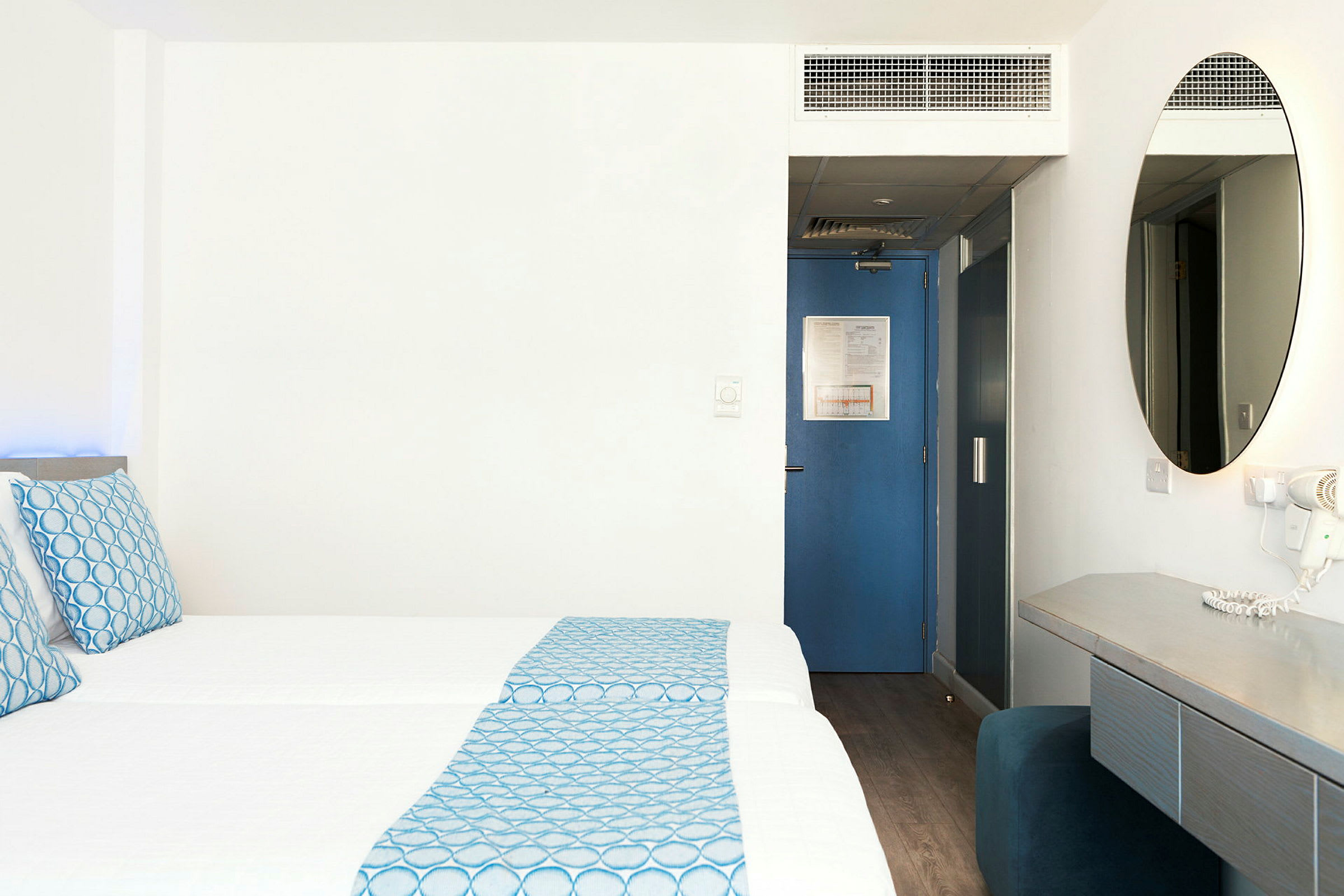 Hotellrum med två bäddar, blå detaljer och skrivbord. (AI-genererad text)