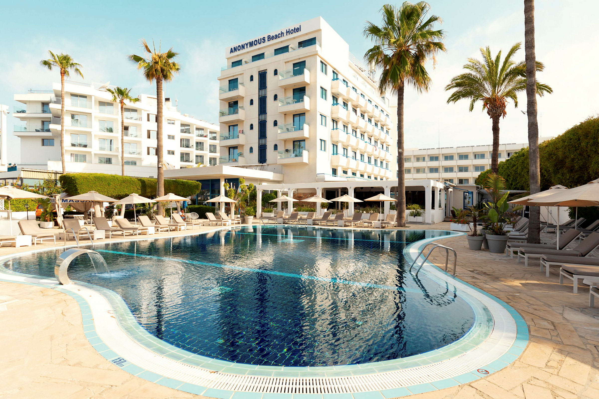 Hotellbyggnad med pool och solstolar omgivna av palmer. (AI-genererad text)