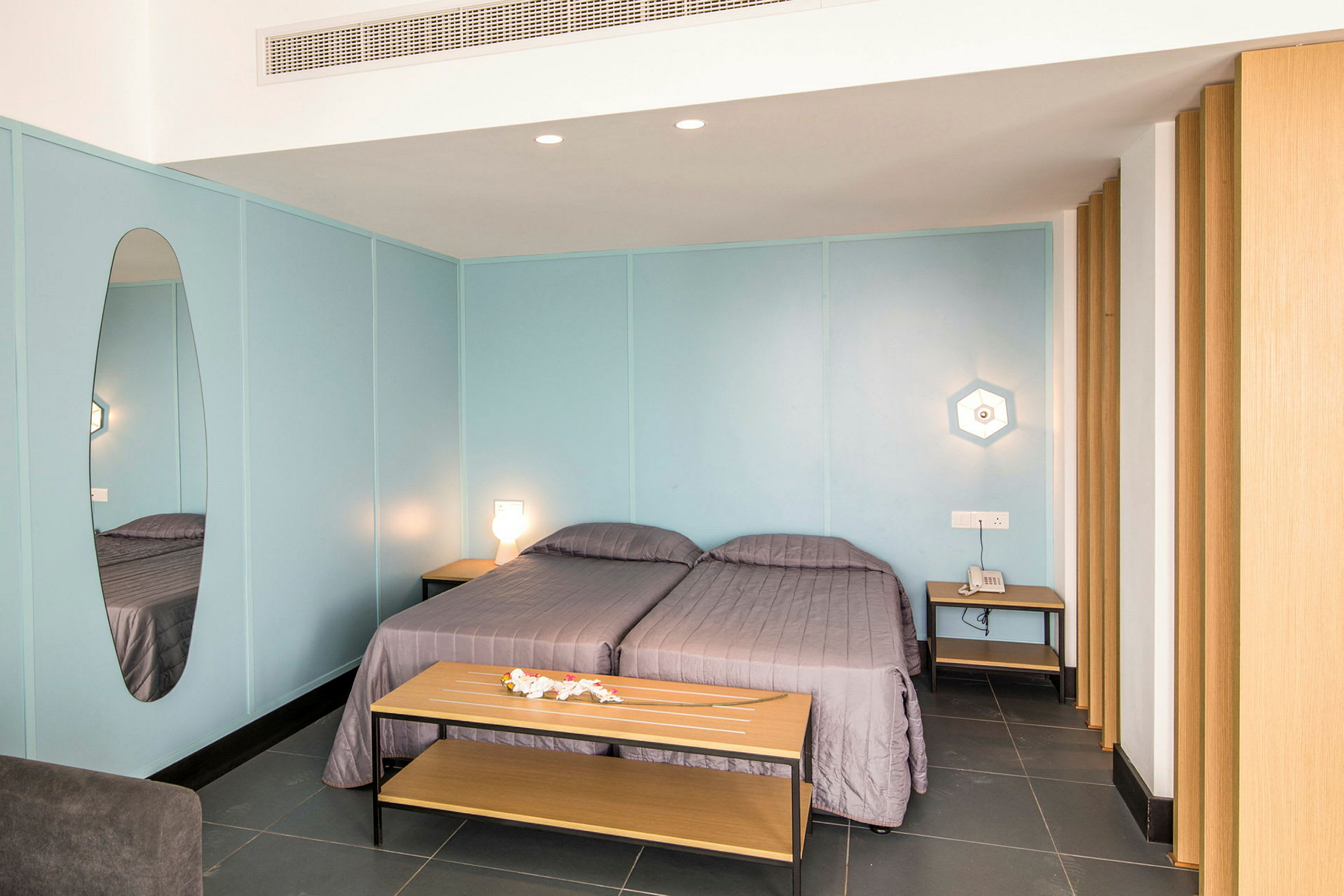Ett hotellrum med blå väggar och två enkelsängar täckta med grå sängkläder. (AI-genererad text)