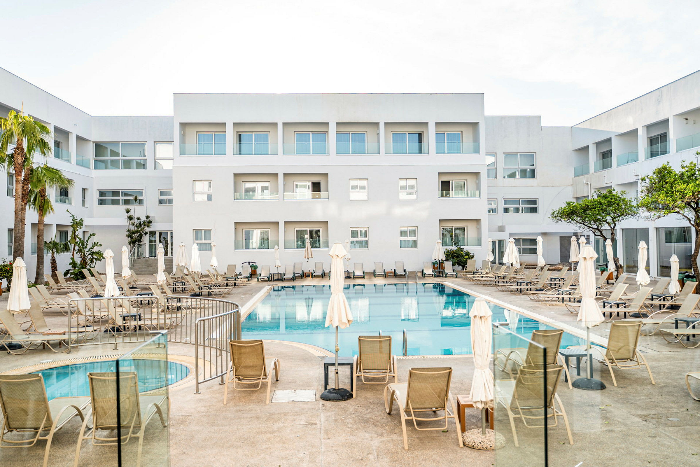 Ett hotell med en utomhuspool och solstolar, omgiven av vita byggnader. (AI-genererad text)