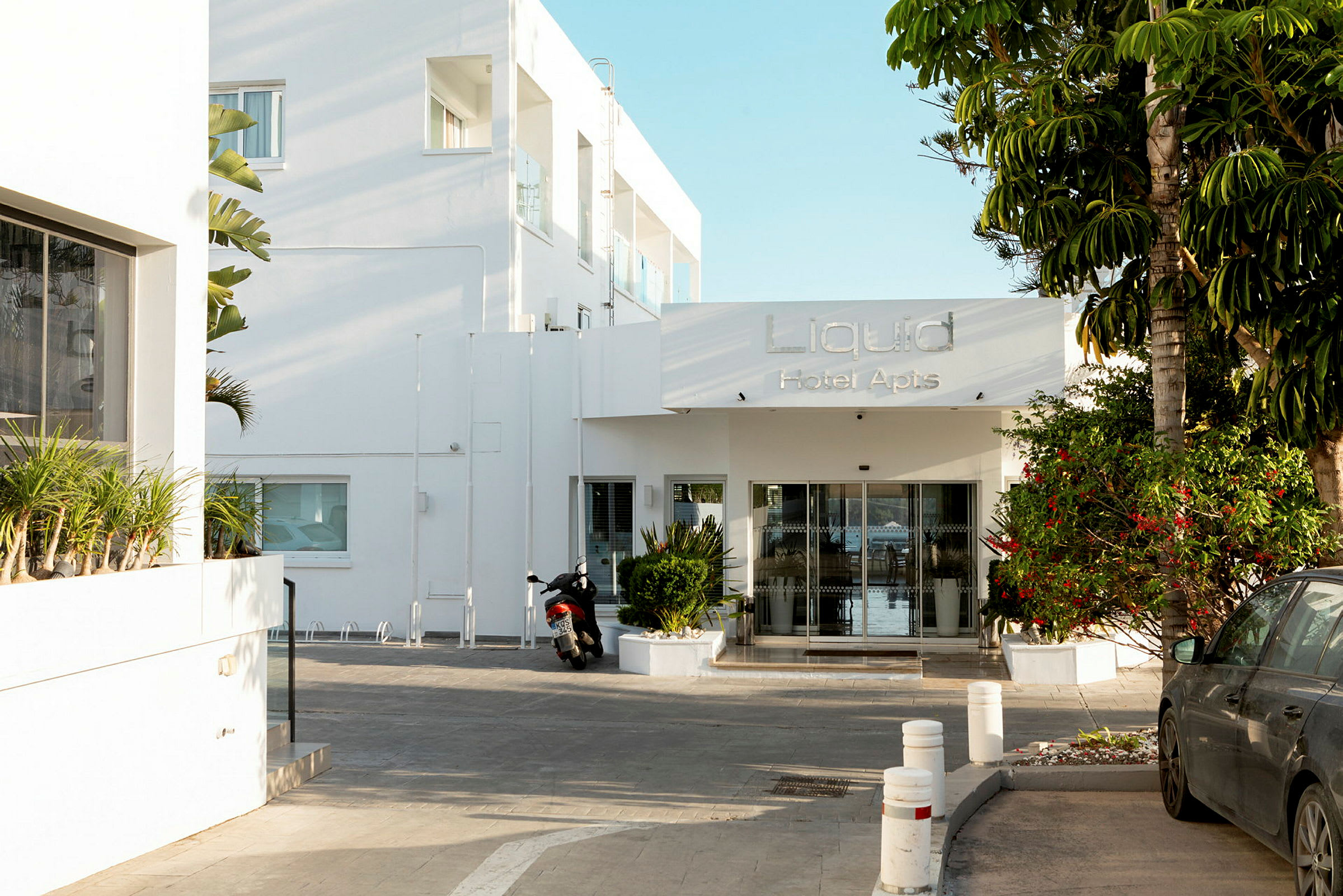 Entré till Liquid Hotel Apartments med en motorcykel och bil framme. (AI-genererad text)