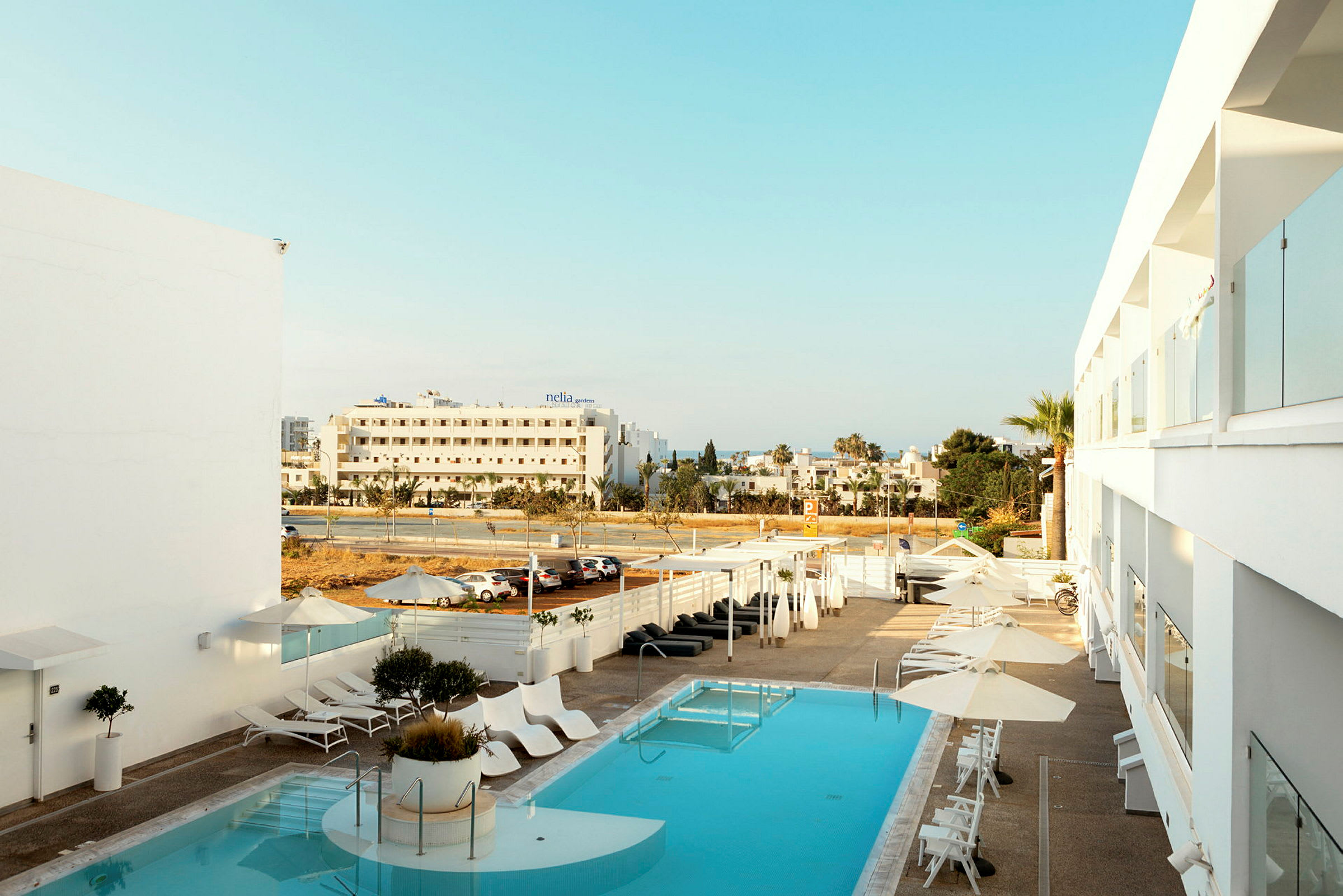 Hotellpool med solstolar och parasoller, vy mot gatan och omgivande byggnader. (AI-genererad text)