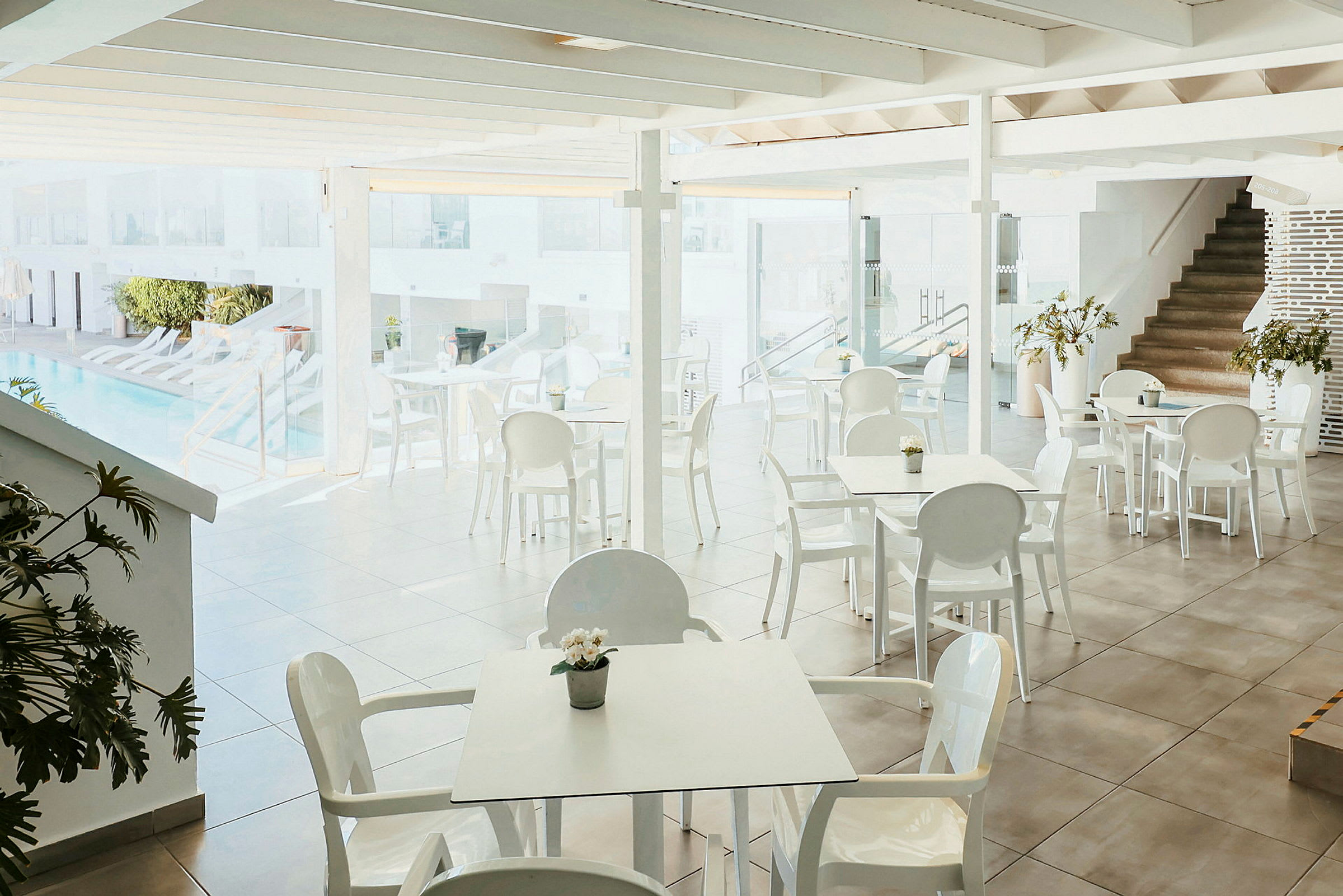 En ljus restaurang med vita bord och stolar nära en pool. (AI-genererad text)
