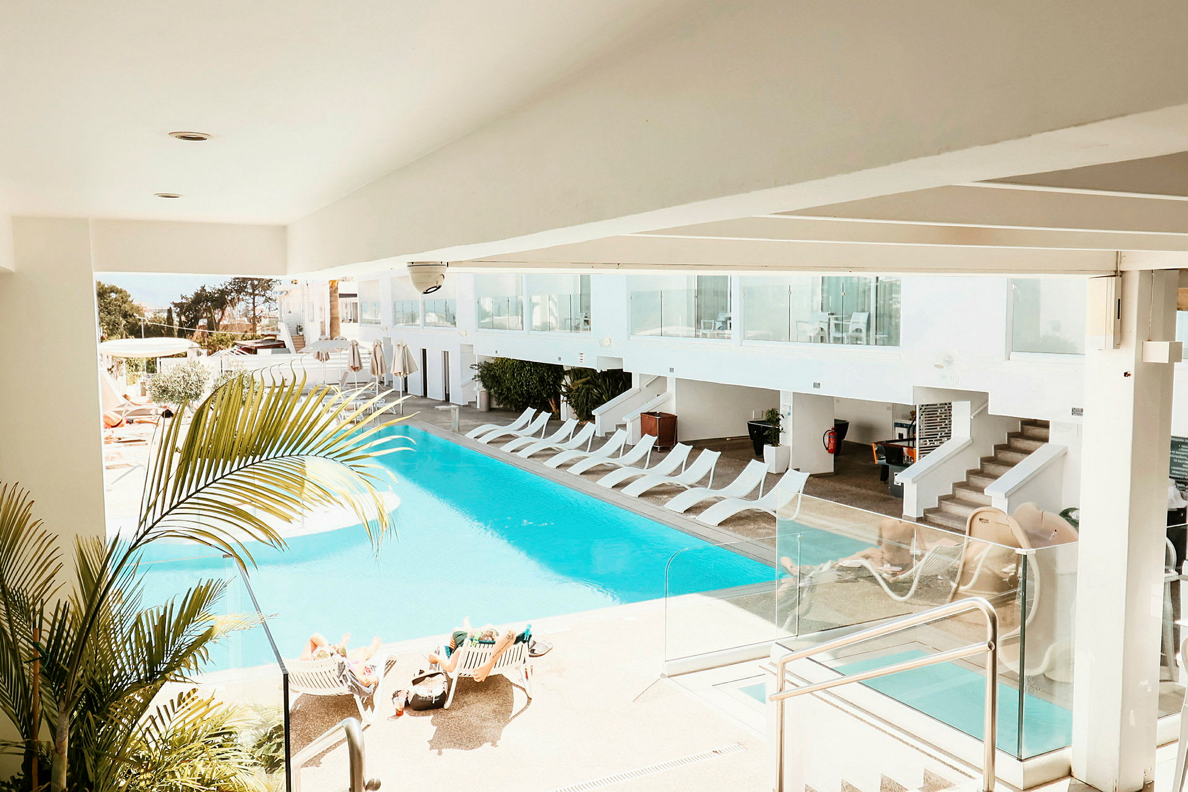 Bild på en ljus hotellpool med solsängar och omgivande grönska. (AI-genererad text)