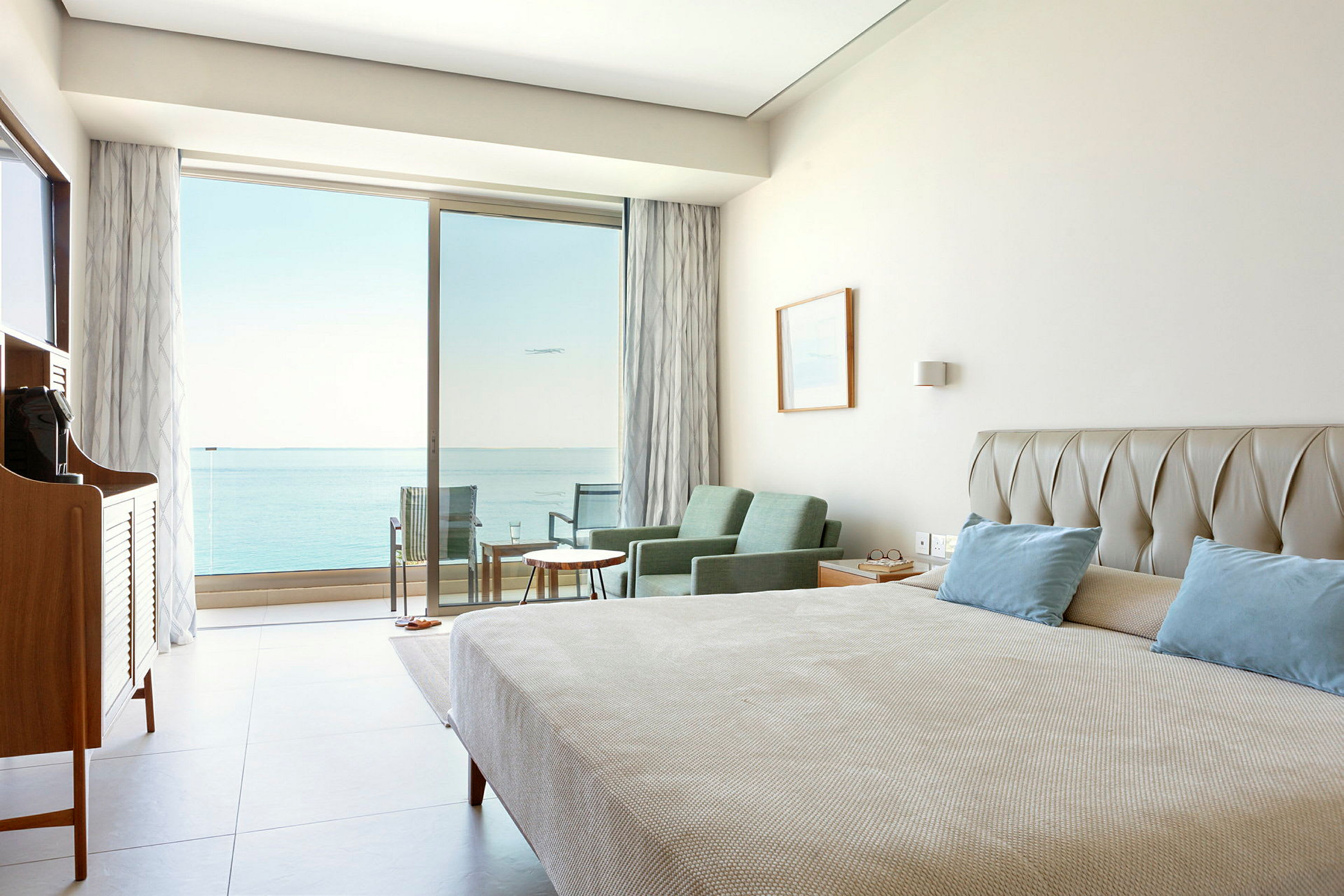 Hotellrum med säng, sittgrupp och utsikt mot havet genom glasdörrar. (AI-genererad text)