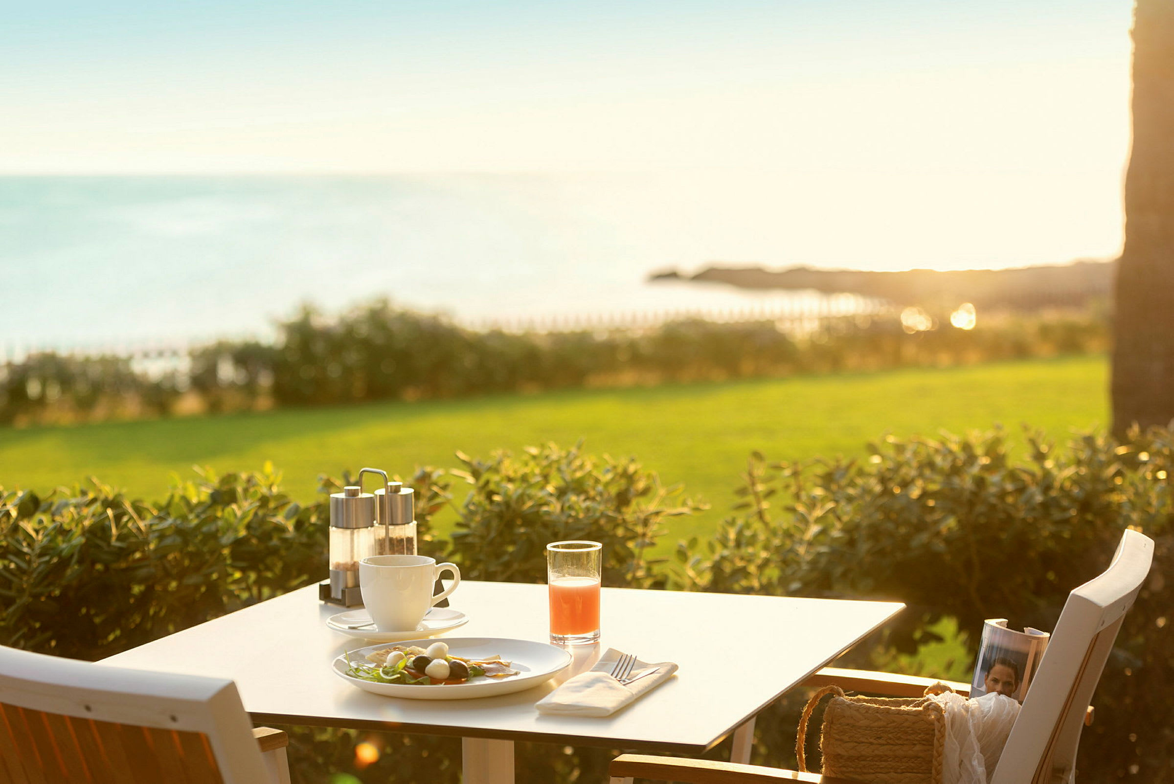 Ett bord med frukost mot en solig utsikt över havet och grönområdet. (AI-genererad text)