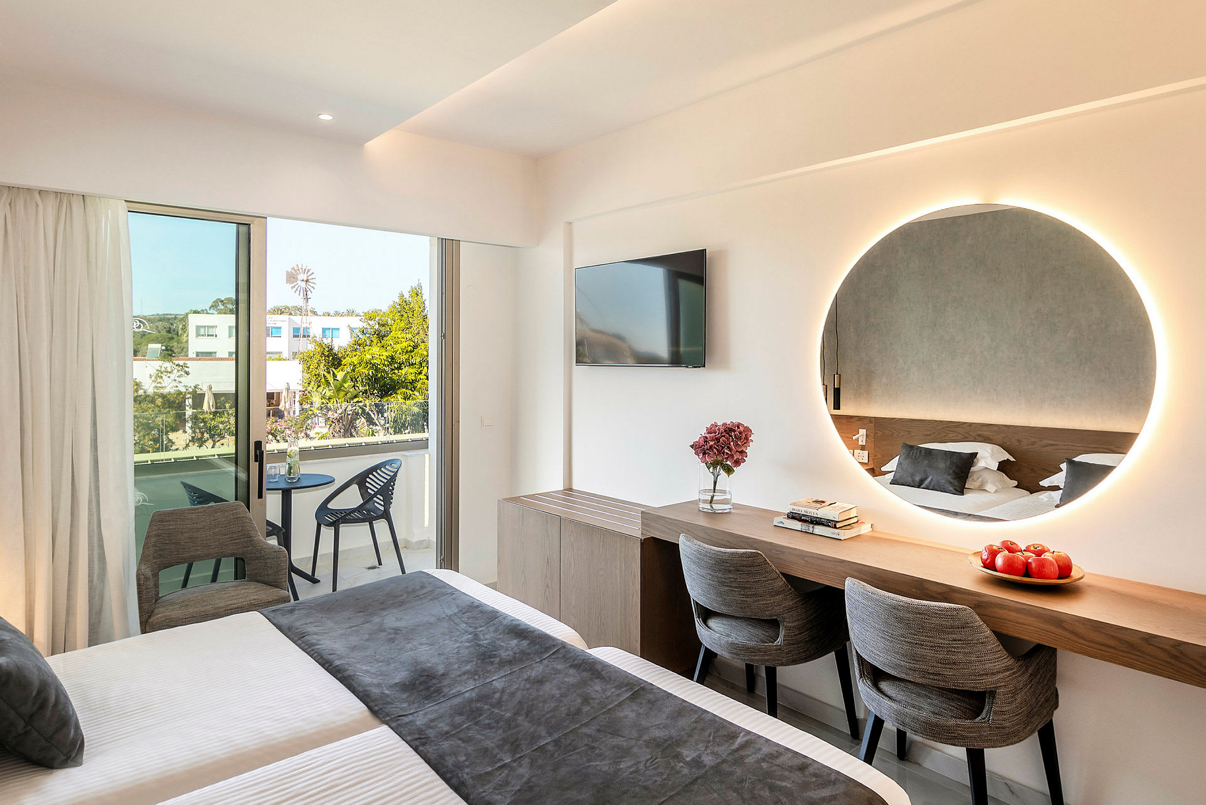 Modernt hotellrum med säng, spegel, skrivbord, stolar och balkong. (AI-genererad text)