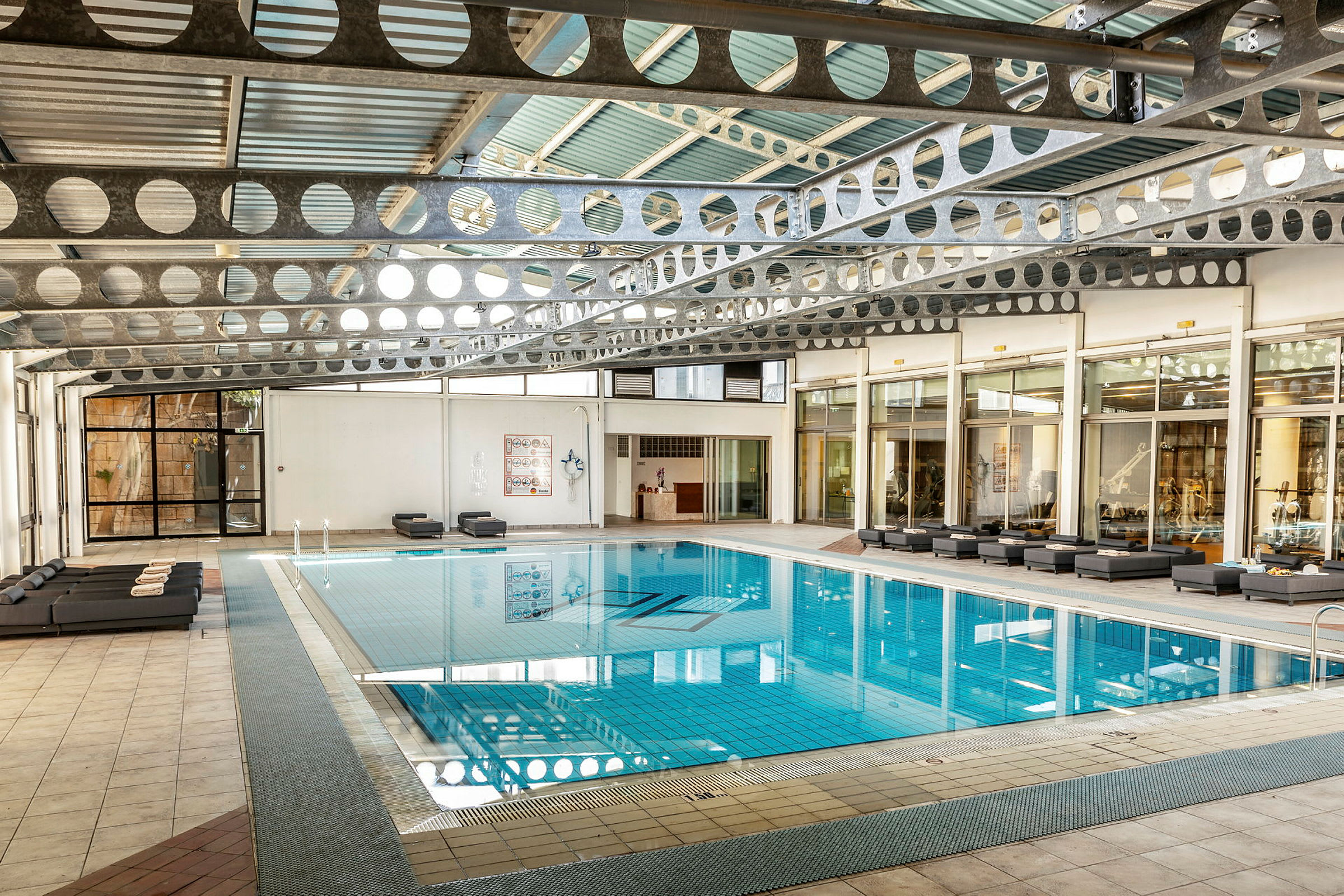En inomhuspool med sittmöbler runt omkring, omgiven av glasväggar. (AI-genererad text)