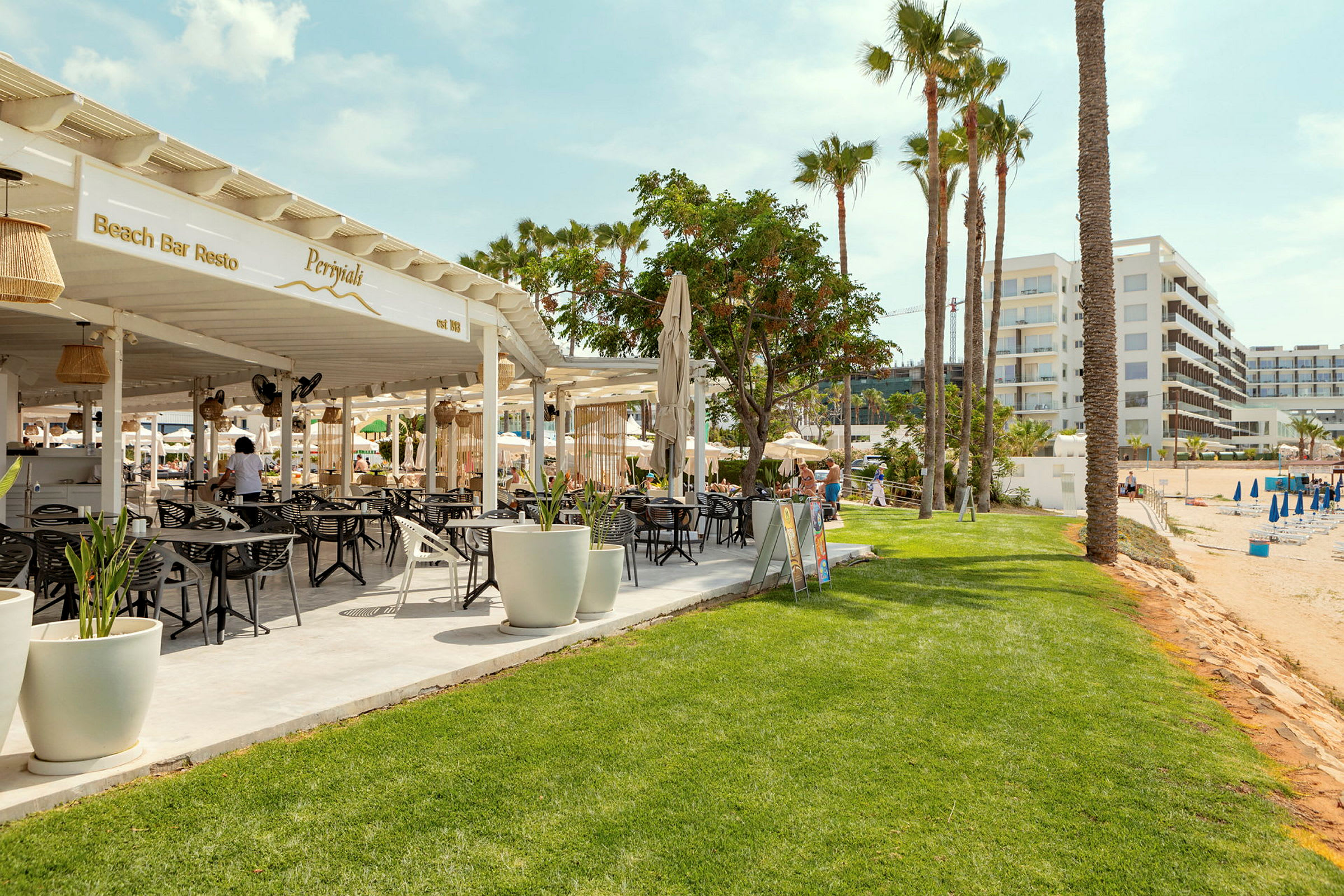 Bild av en strandbar med sittplatser och parasoller samt hotellbyggnader i bakgrunden. (AI-genererad text)