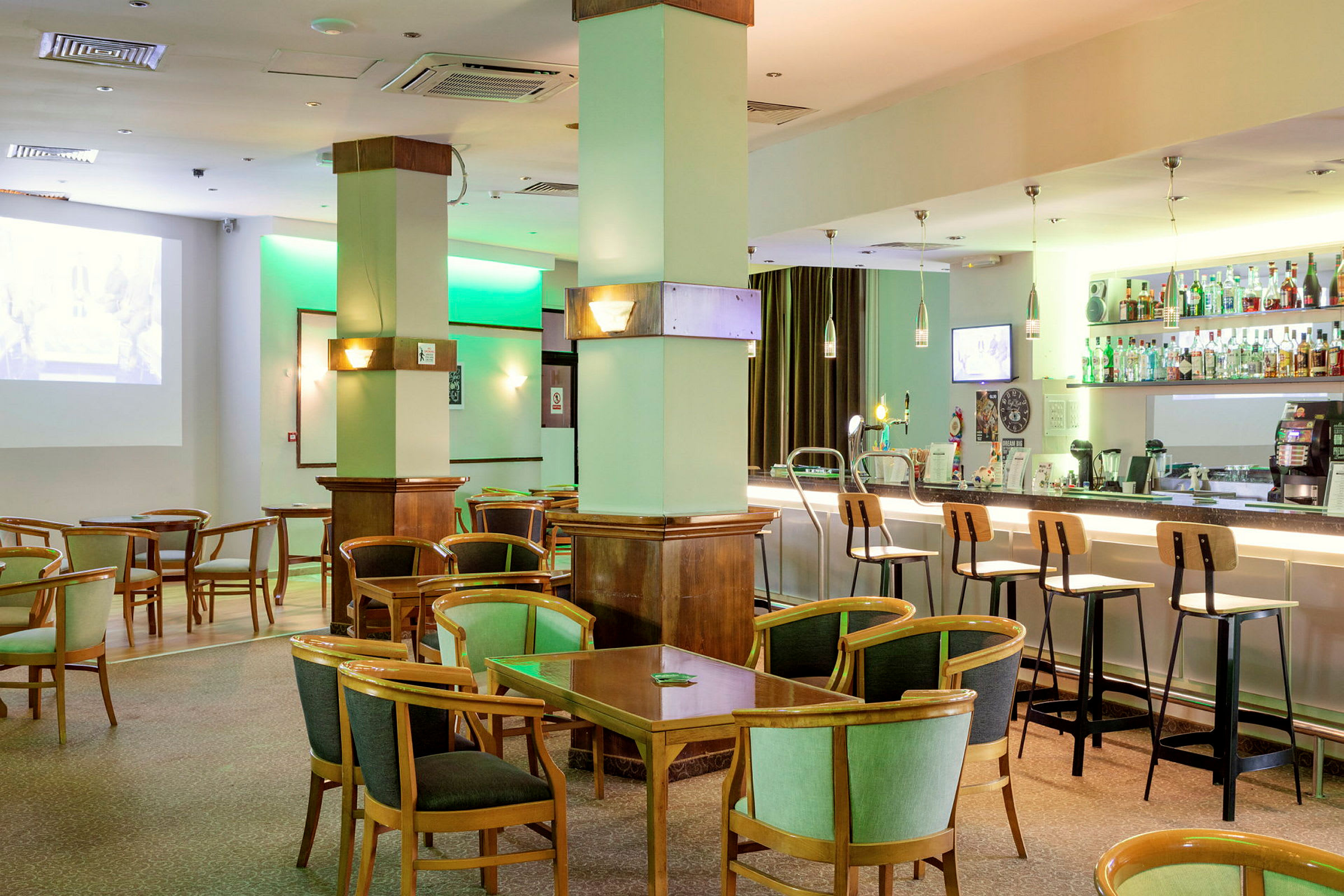 En hotellbar med sittplatser och bord samt hyllor fyllda med flaskor bakom bardisken. (AI-genererad text)