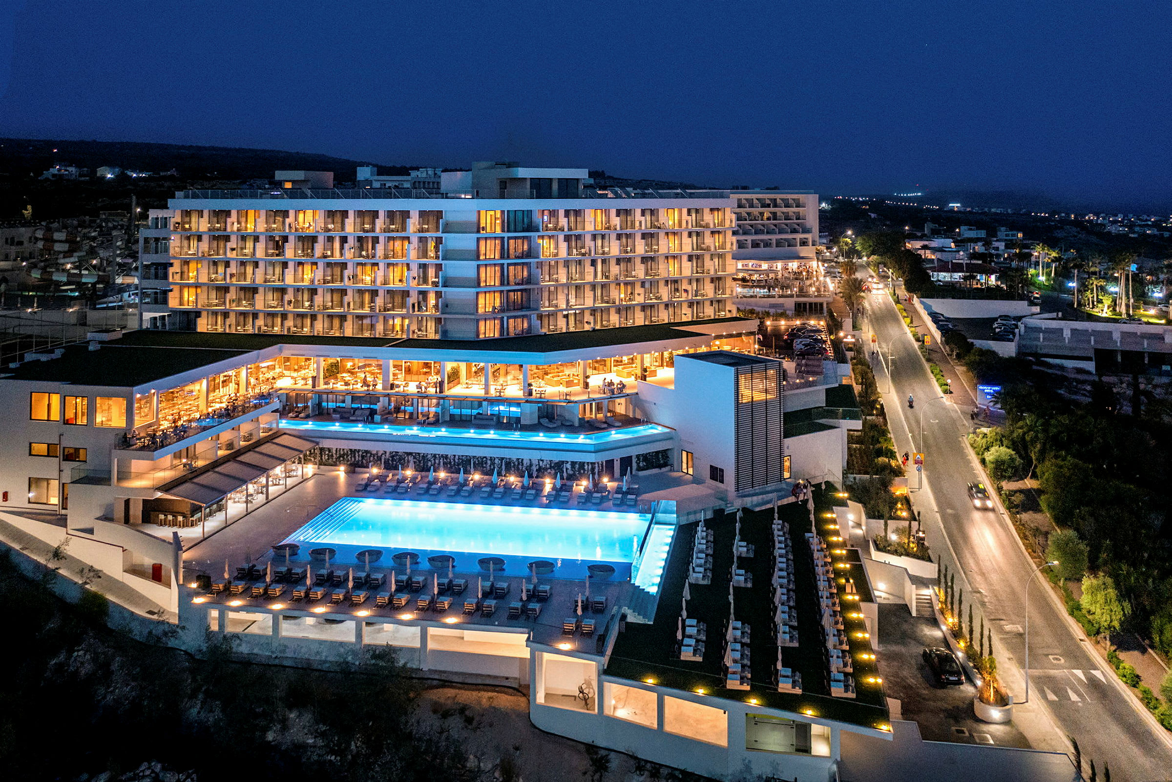 Hotellbyggnad på kvällen med upplyst poolområde. (AI-genererad text)