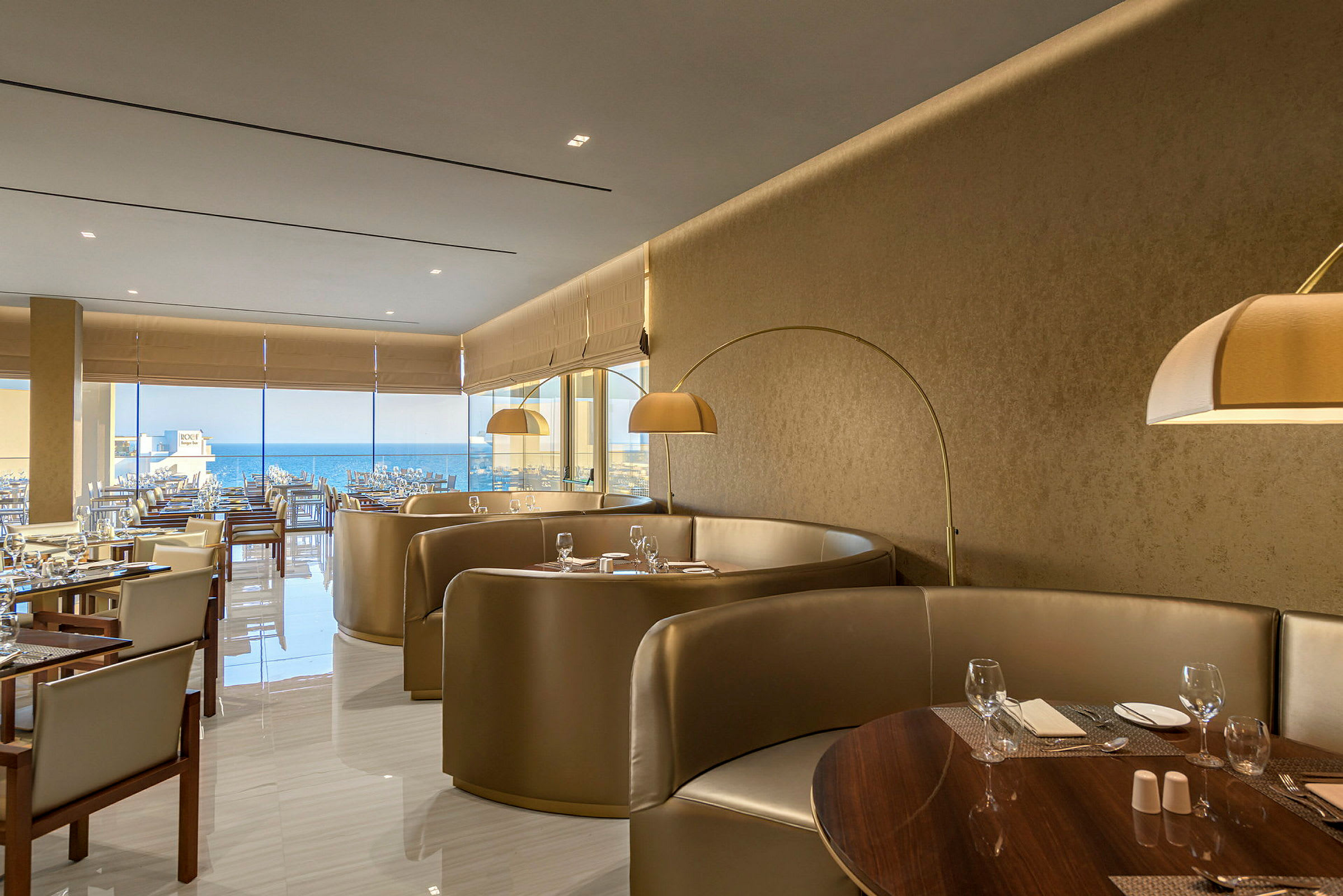 En elegant restaurang med sittgrupper och bord dukade med glas och bestick samt en vy över havet. (AI-genererad text)