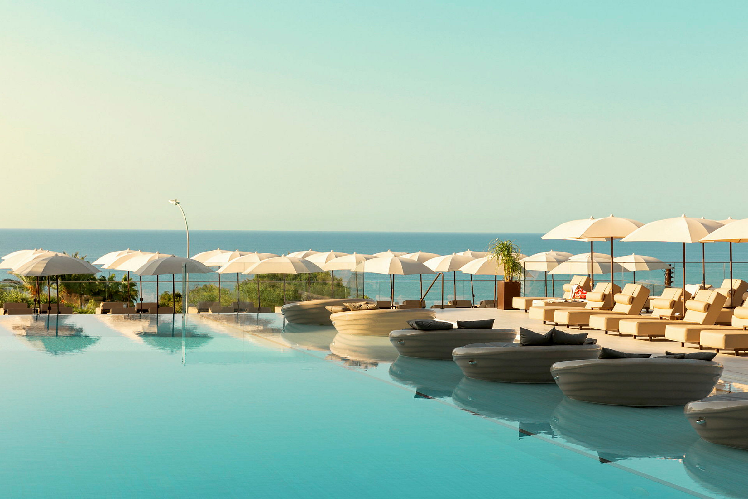 En infinitypool med liggstolar och parasoller vid havet. (AI-genererad text)