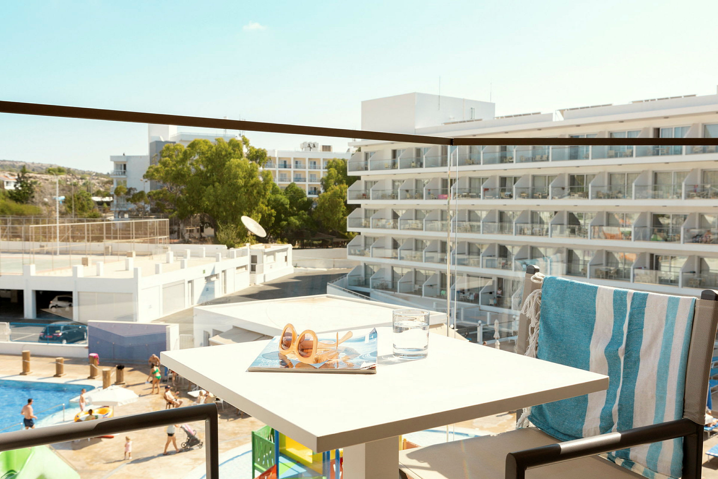 Utsikt från en balkong mot en hotellbyggnad med balkonger och människor vid en pool. (AI-genererad text)