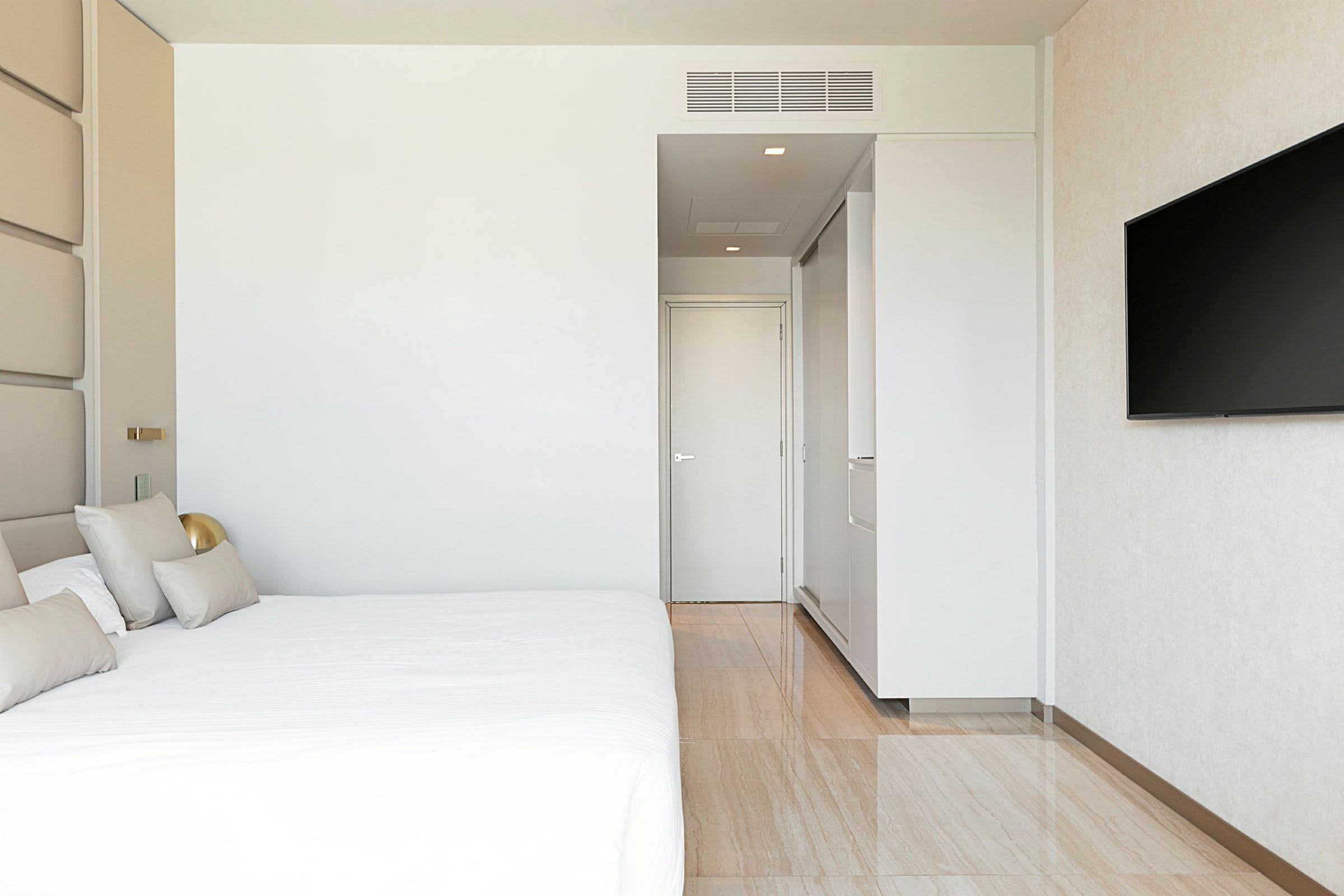 Ett modernt hotellrum med en stor säng, vit vägg, en dörr och en väggmonterad TV. (AI-genererad text)