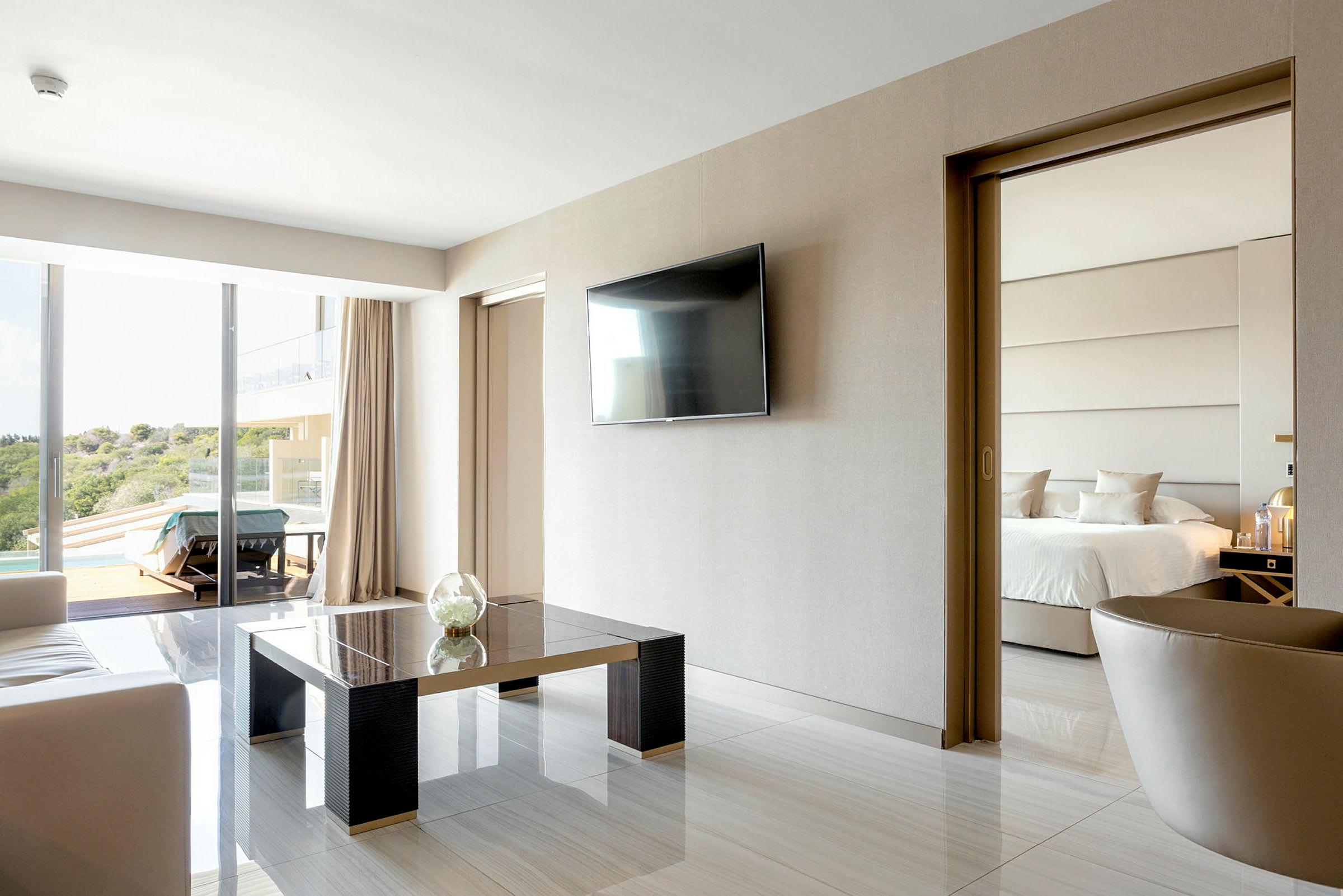 Modernt hotellrum med sittgrupp, TV på väggen och skjutdörr till sovrummet med en dubbelsäng. (AI-genererad text)