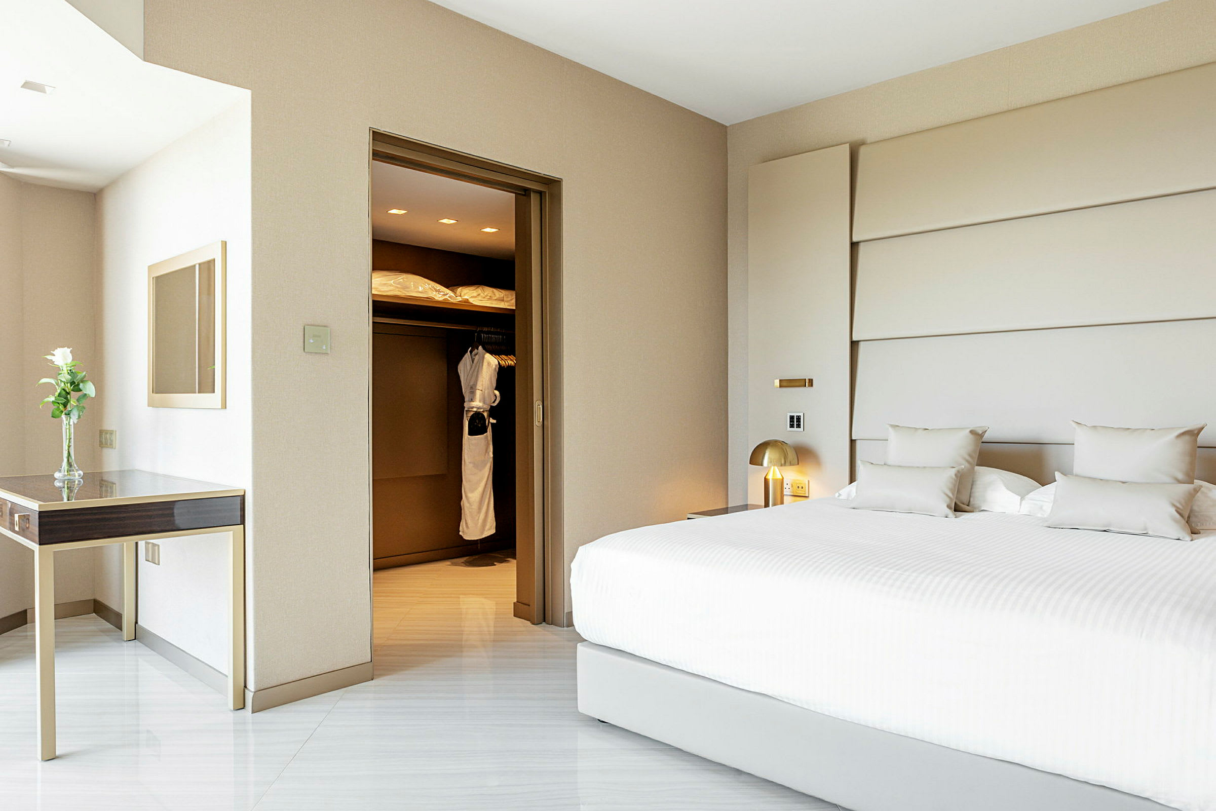 Hotellrum med en stor vit säng, ett skrivbord med en vas och en garderob innehållande morgonrockar. (AI-genererad text)