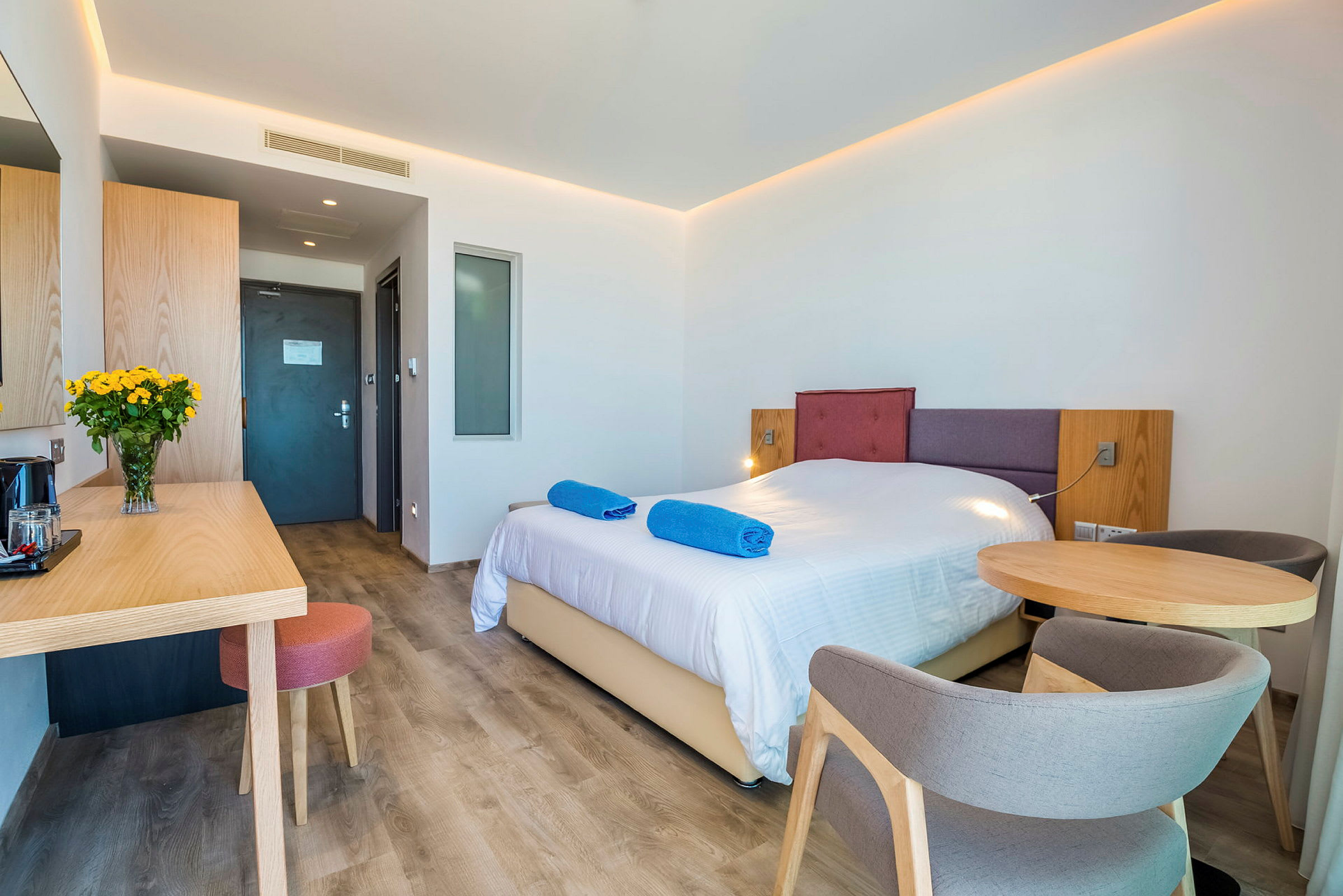 Hotellrum med en dubbelsäng, ett bord med stolar och en skrivbordsyta. (AI-genererad text)
