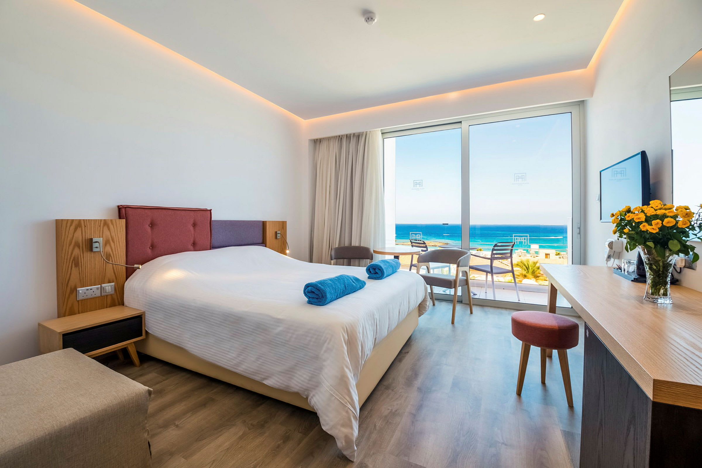 Hotellrum med en dubbelsäng, sittgrupp och utsikt över havet. (AI-genererad text)