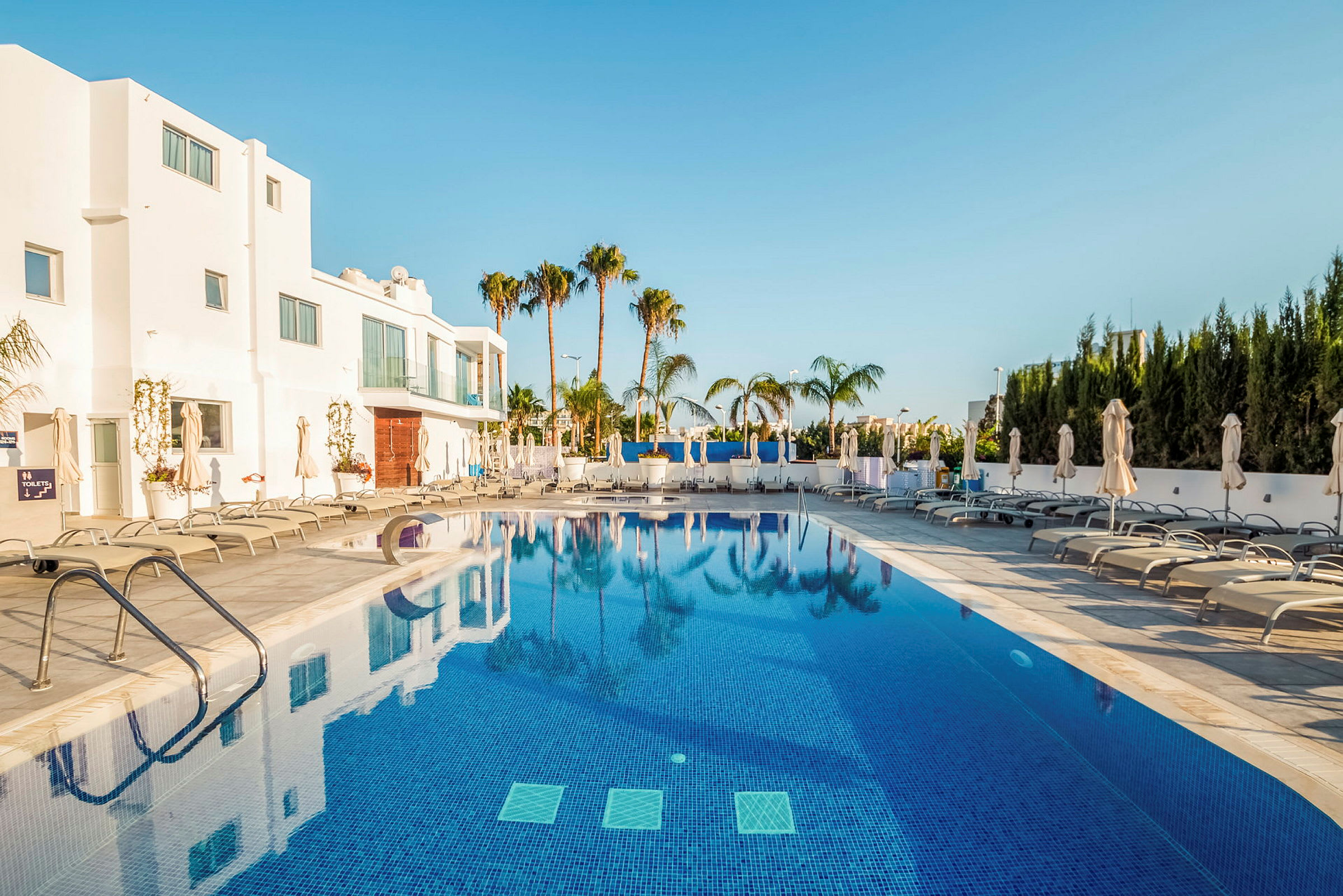 Utomhuspool vid hotell med solsängar och parasoller. (AI-genererad text)