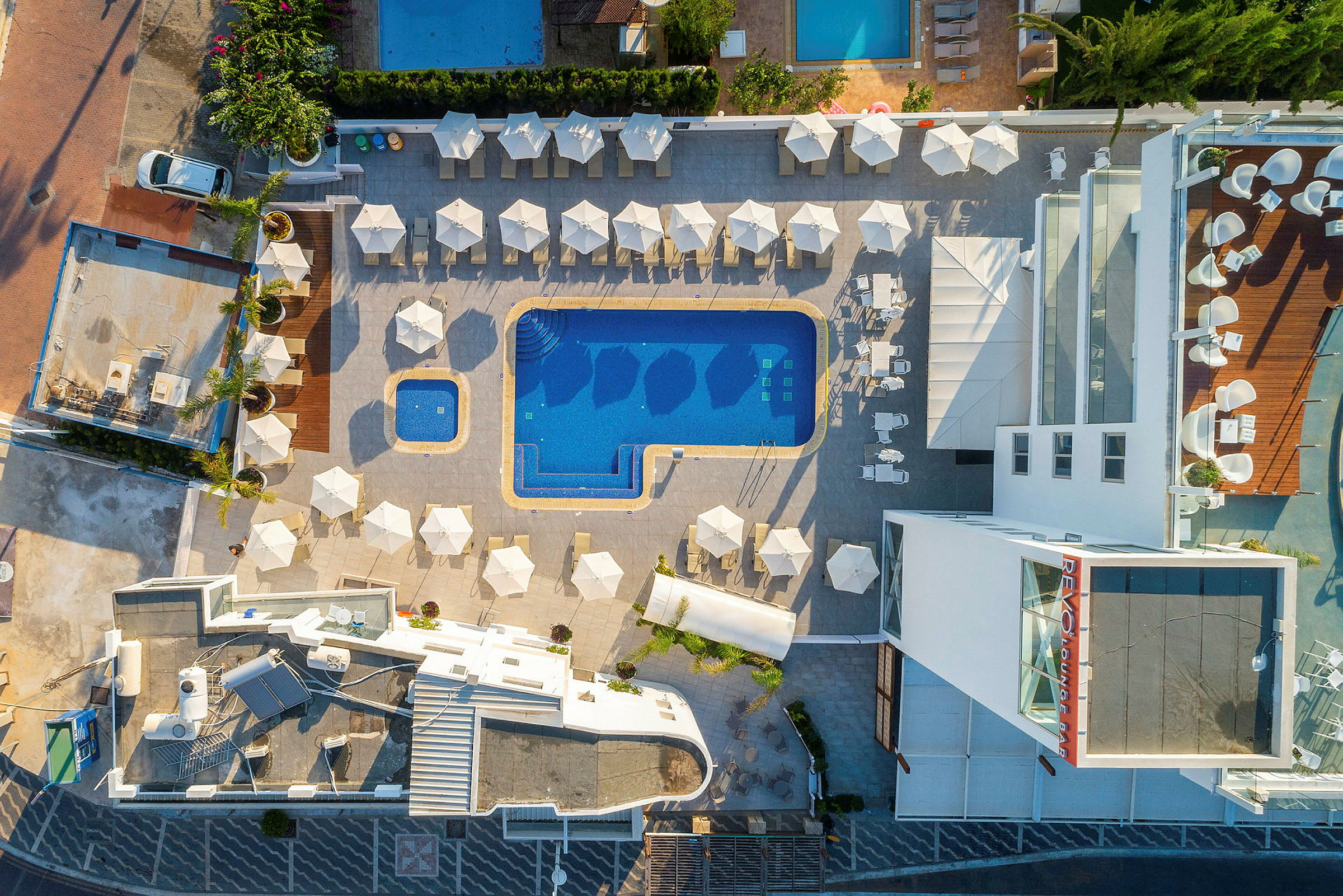 Flygfoto av poolområdet på ett hotell med solstolar och parasoller. (AI-genererad text)