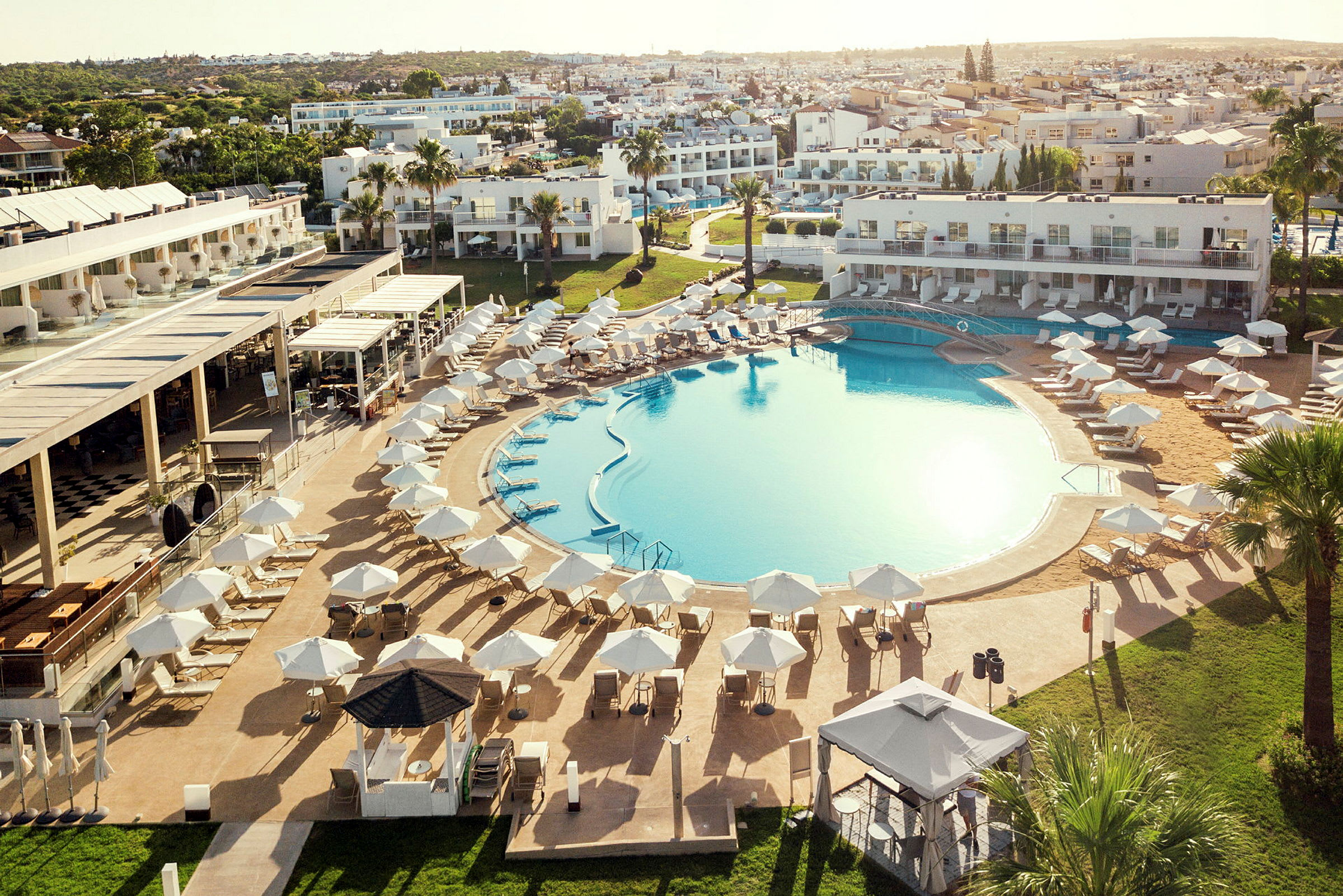 En stor utomhuspool omgivet av solstolar och parasoller, med hotellbyggnader i bakgrunden. (AI-genererad text)