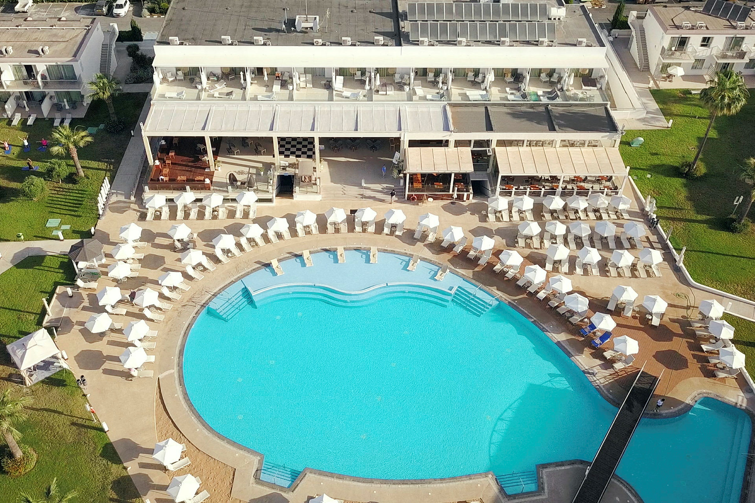 Fågelfoto av hotellområde med stor pool och solstolar. (AI-genererad text)