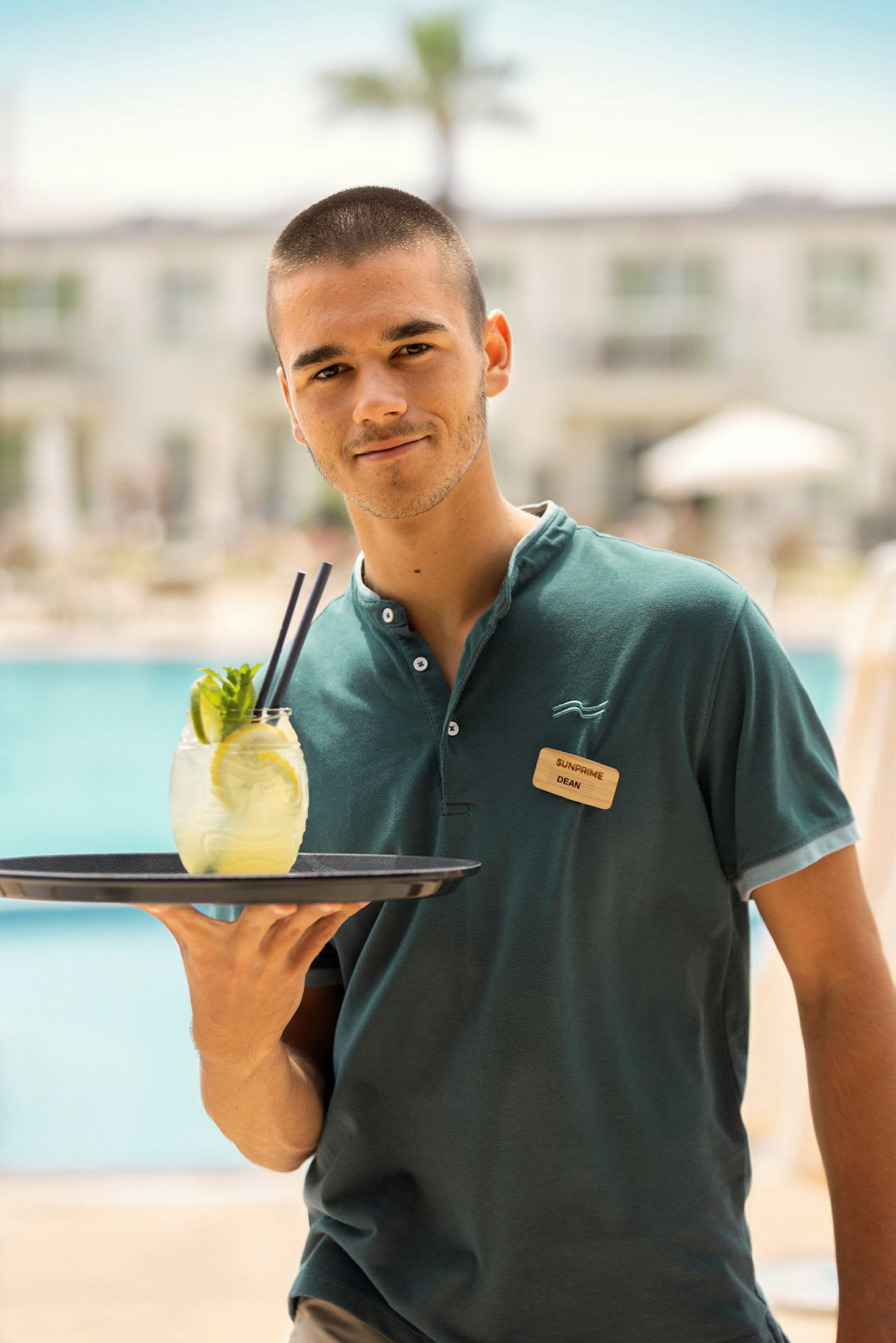 Person i uniform som bär en bricka med en drink vid en pool. (AI-genererad text)