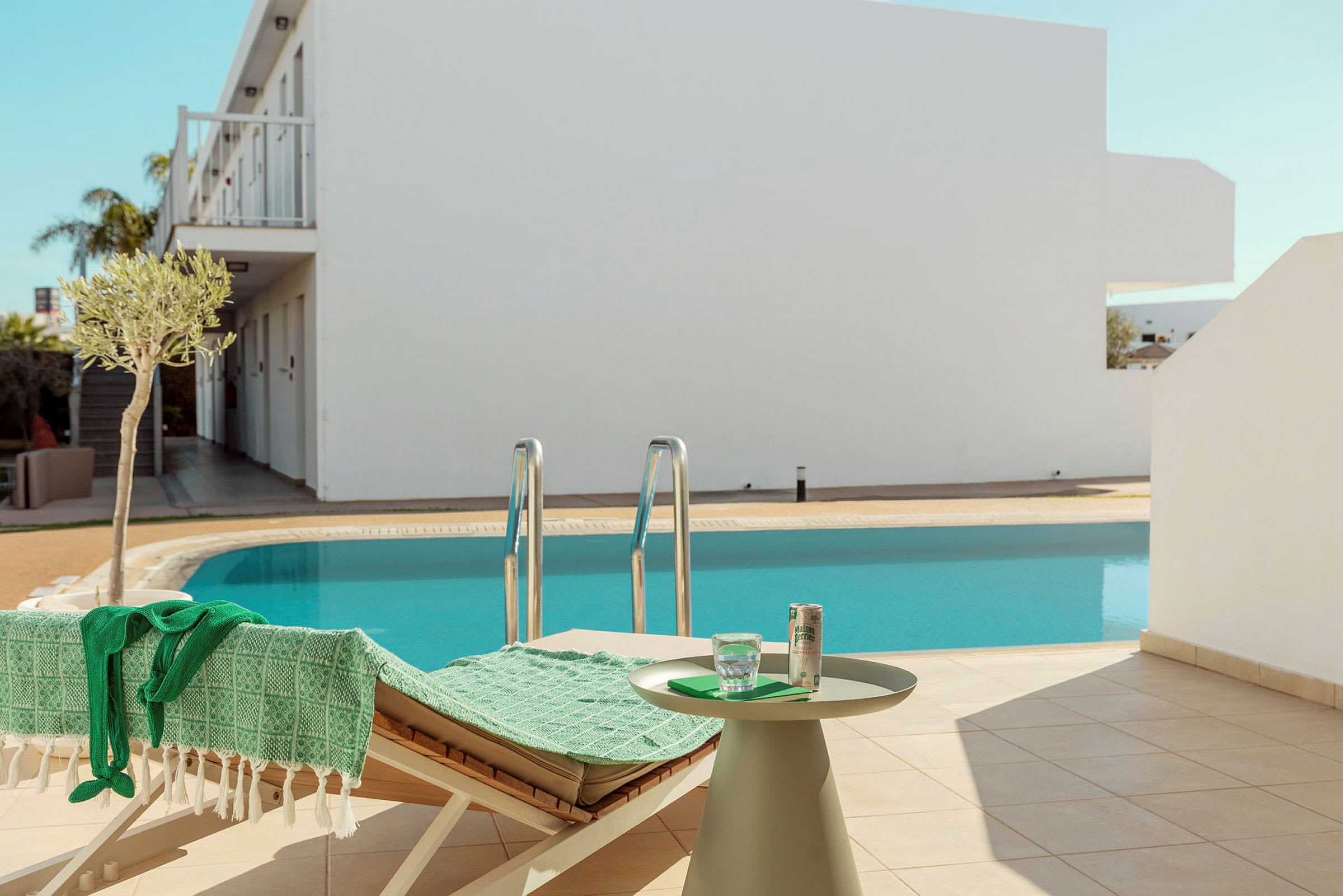 En swimmingpool med en solstol och ett bord med drycker i förgrunden. (AI-genererad text)
