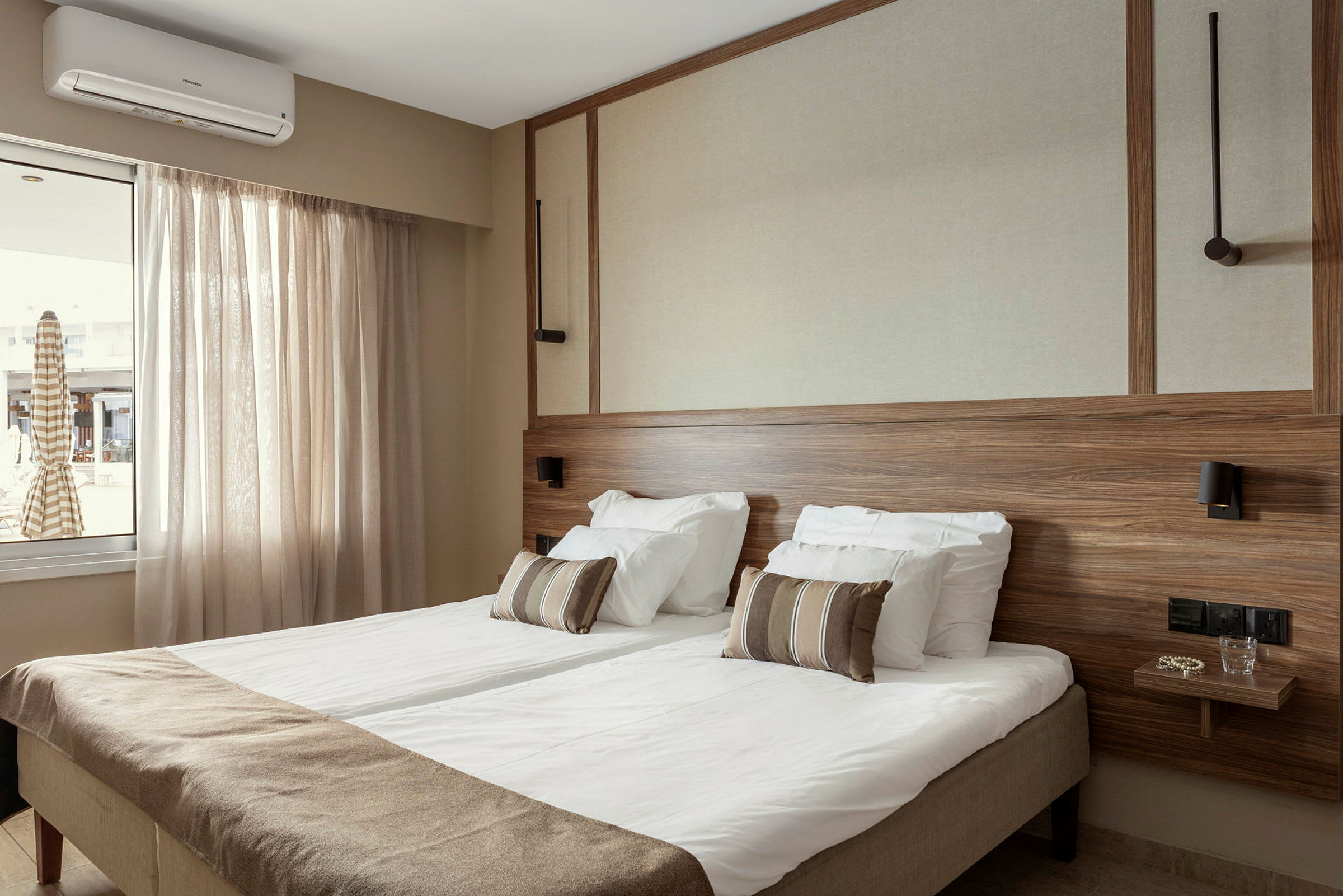 Hotellrum med dubbelsäng, ljusa gardiner, träpaneler och fönster med utsikt. (AI-genererad text)