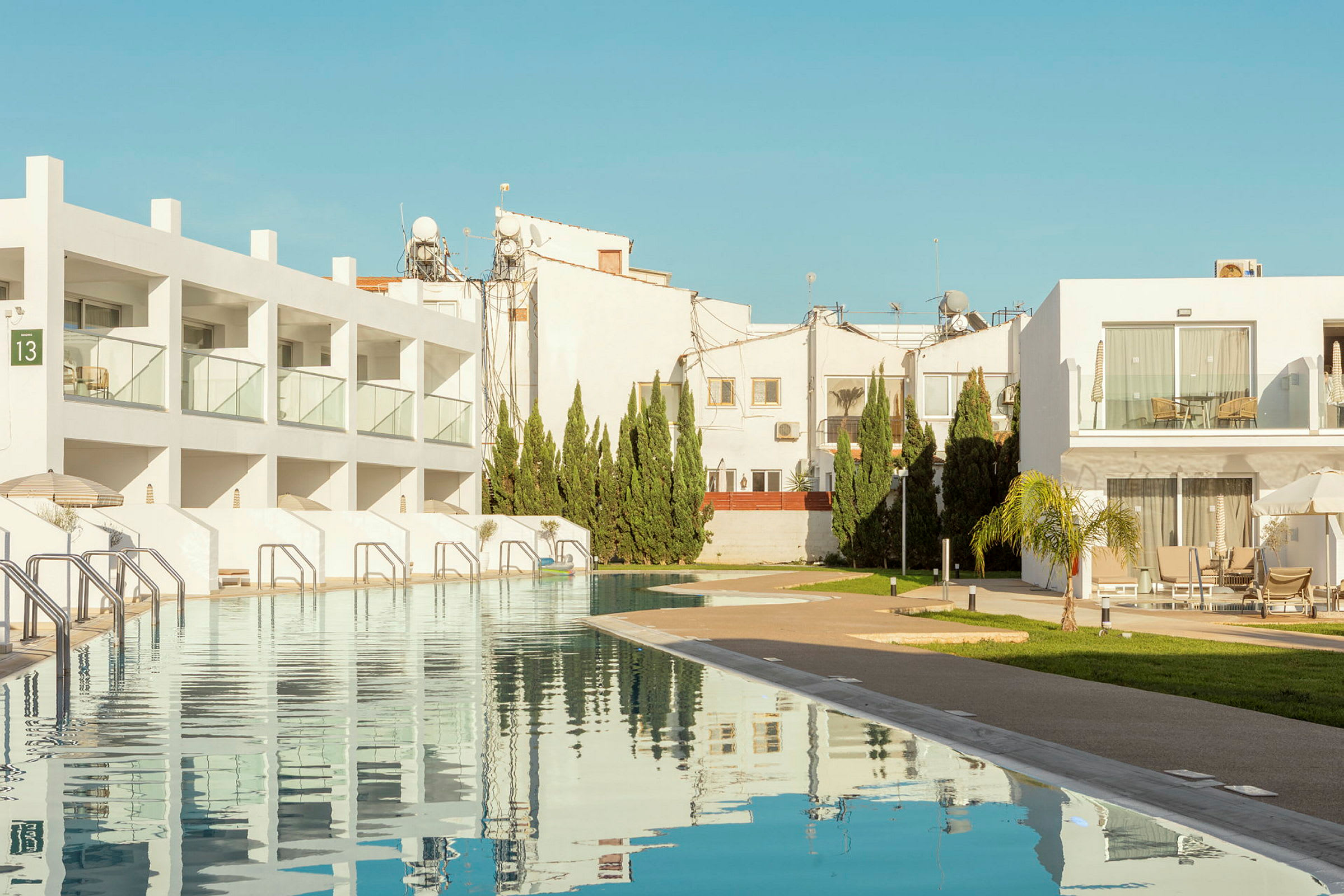 Bilden visar ett modernt semesterkomplex med vita byggnader, en pool och grönska. (AI-genererad text)