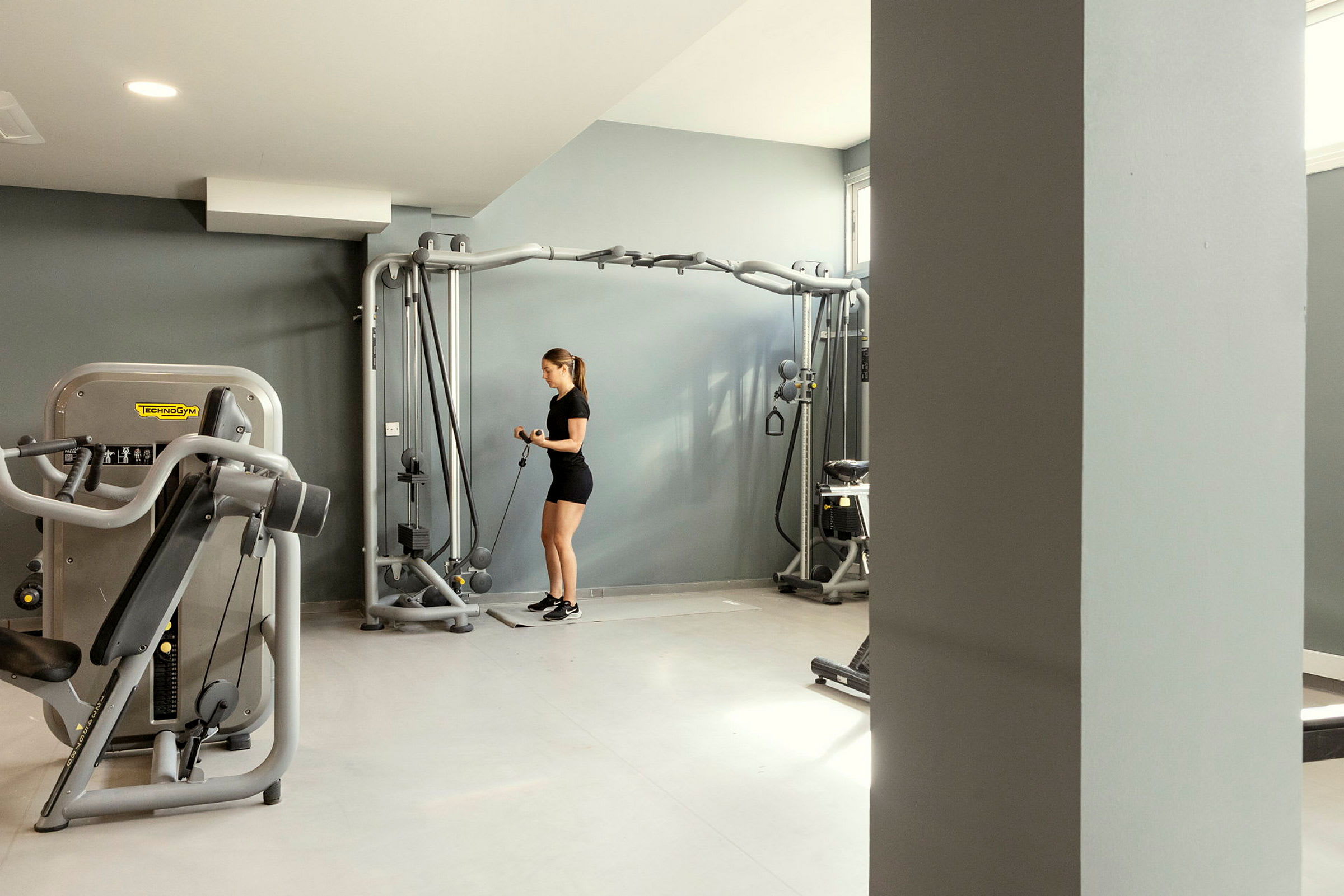 Gym med träningsmaskiner och en person som använder utrustning. (AI-genererad text)