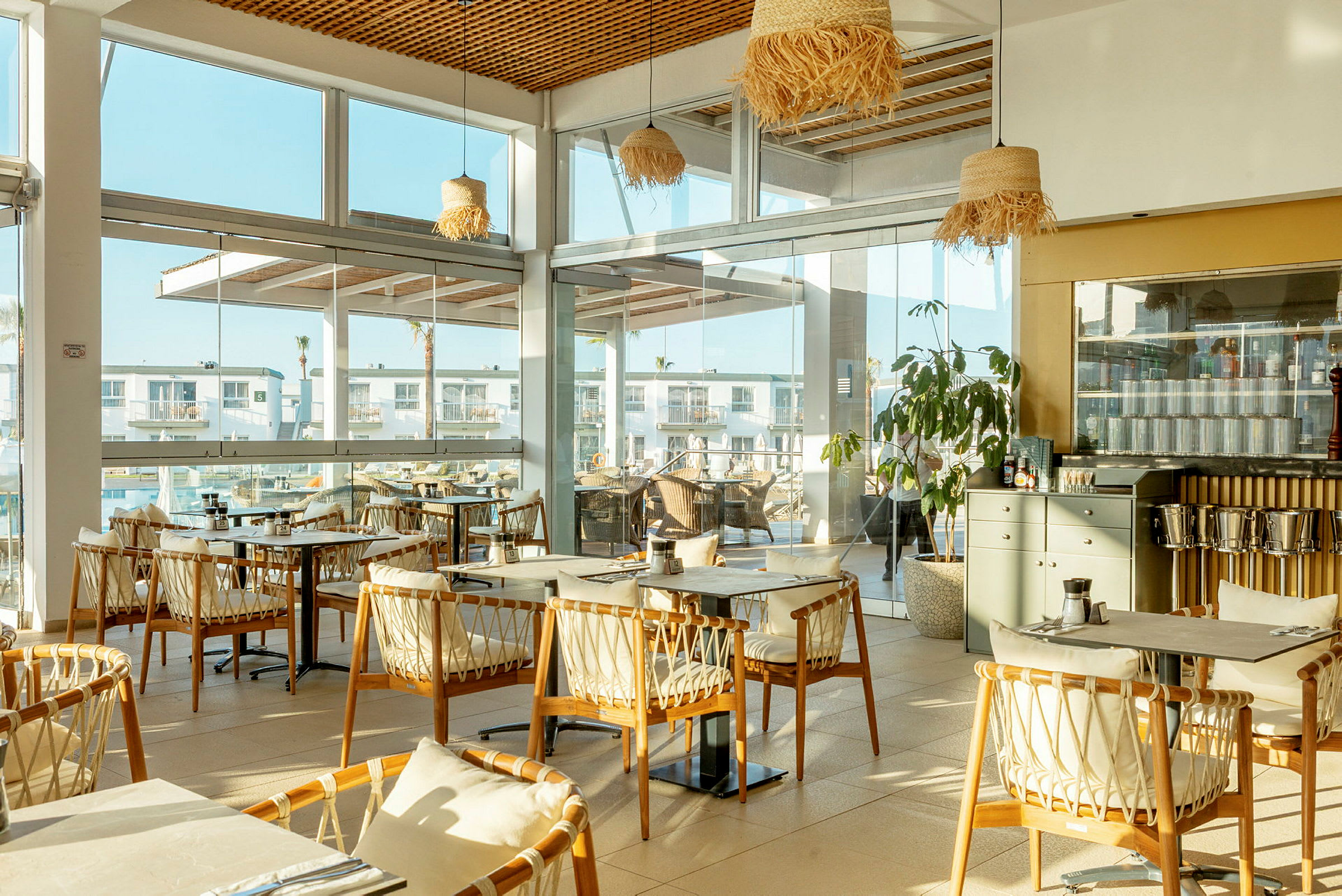 En restaurang med stora fönster och trästolar kring bord. (AI-genererad text)