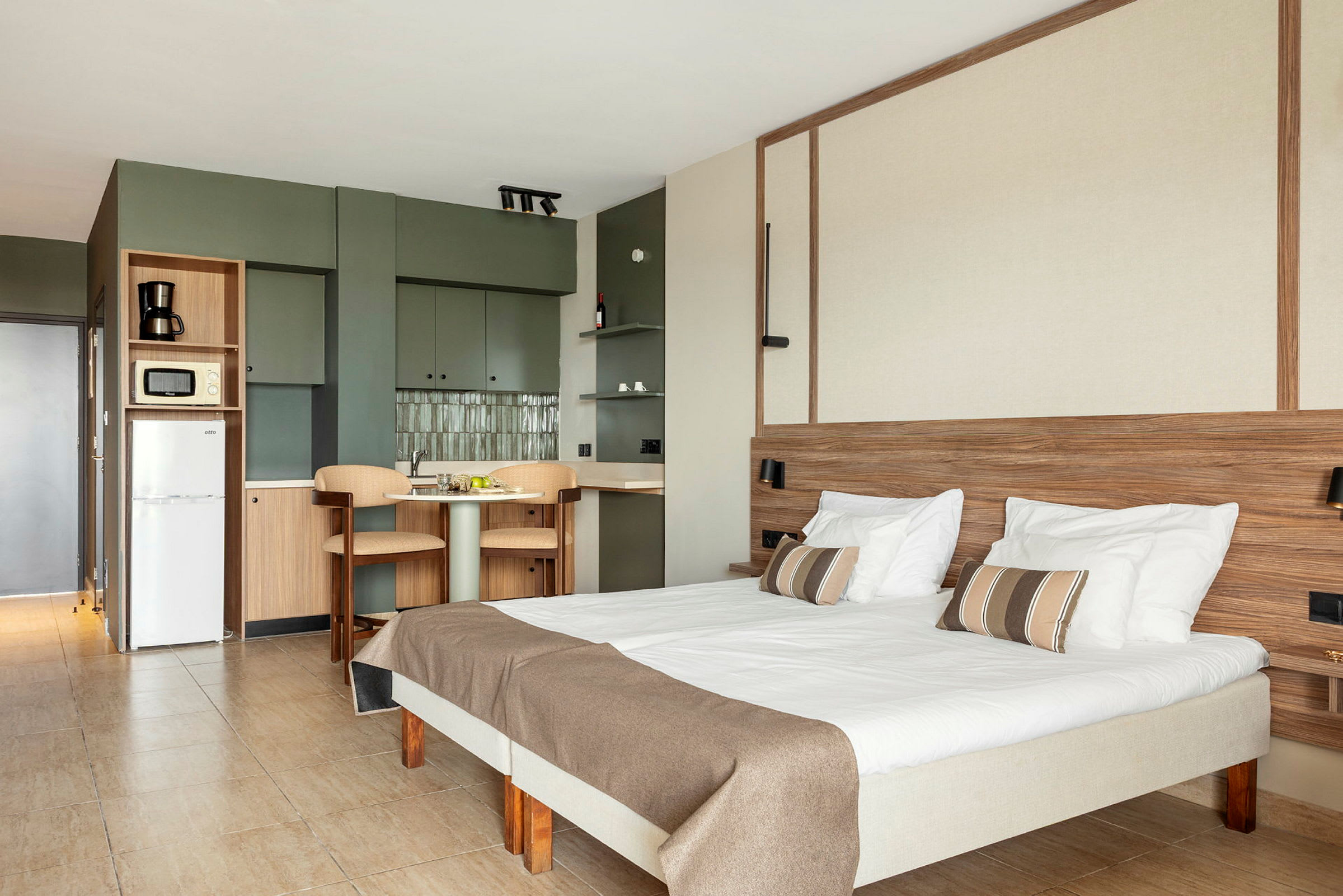 Inomhusbild av ett ljust och modernt hotellrum med en säng, bord, stolar och köksdel. (AI-genererad text)