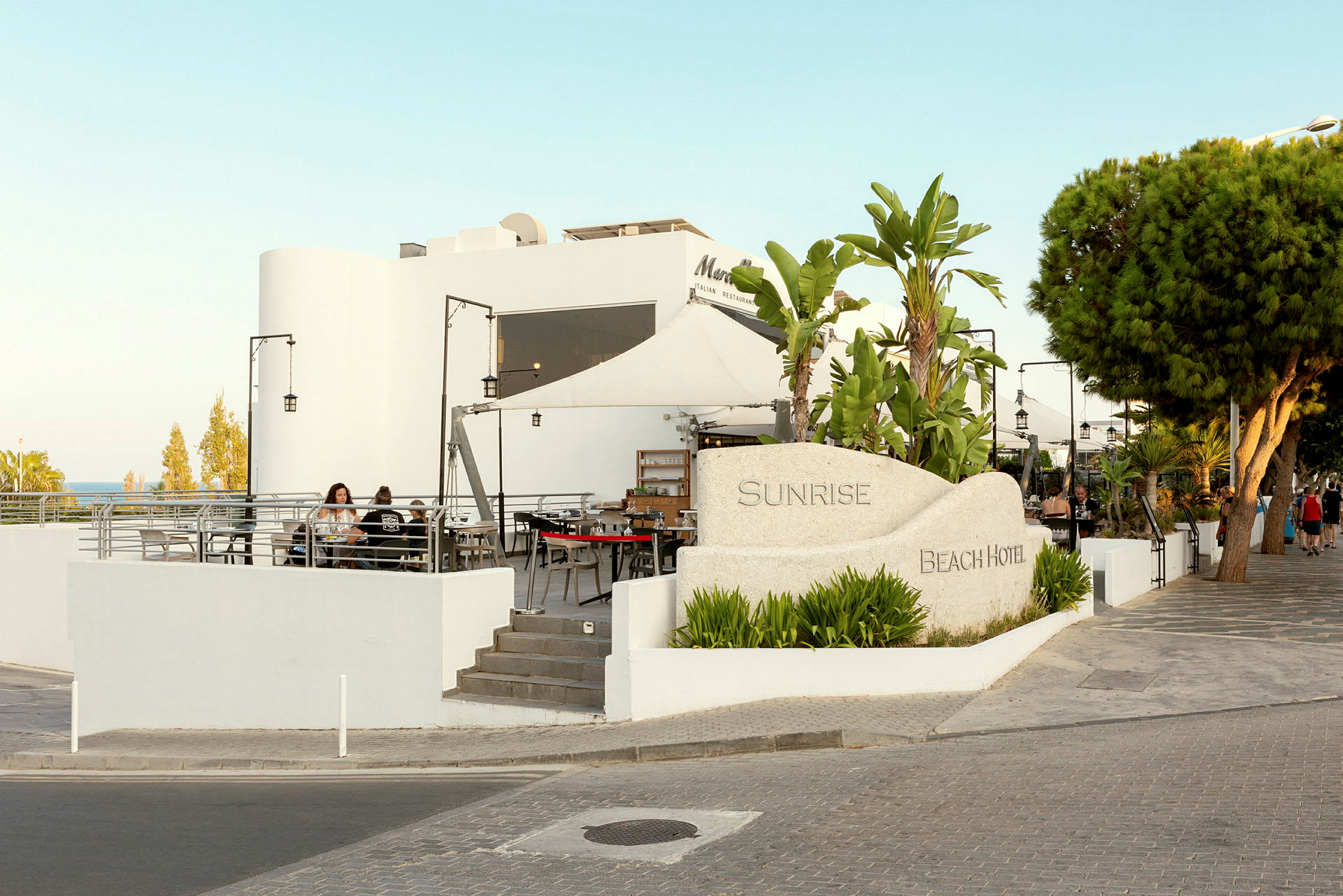 Hotell Sunrise Beach med uteservering och träd i omgivningen. (AI-genererad text)