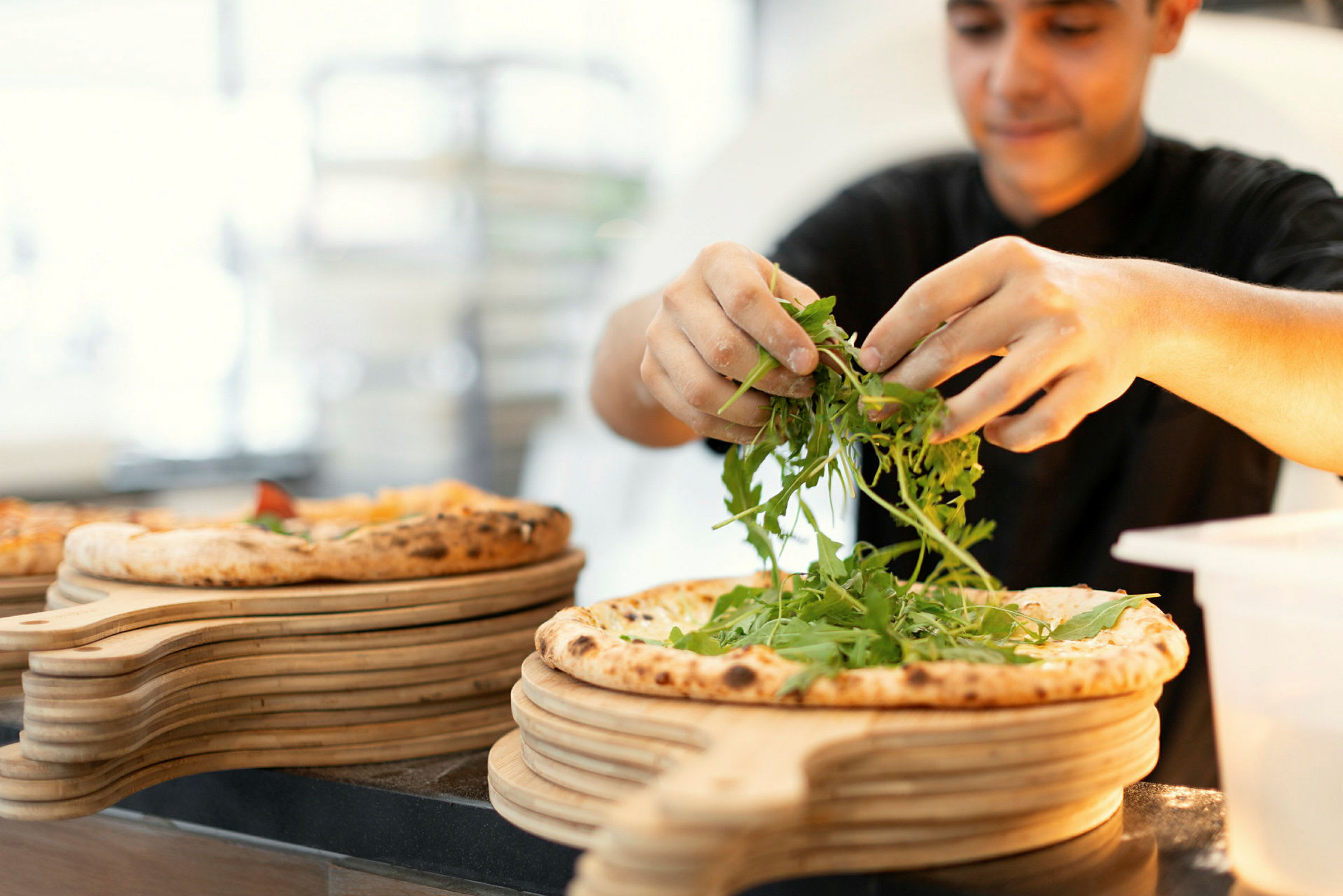 En person dekorerar en pizza med ruccolasallad. (AI-genererad text)