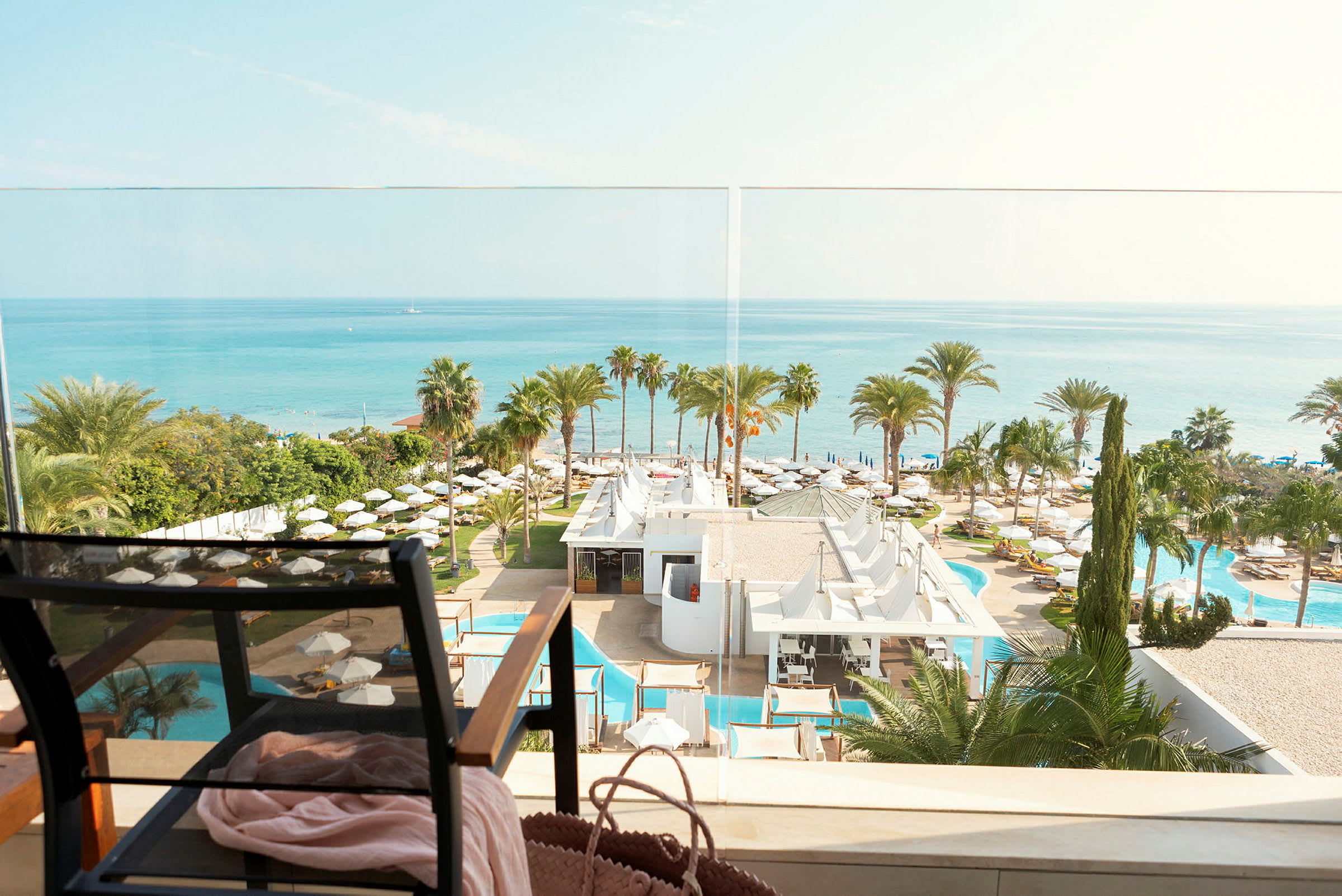 Utsikt över havet, hotellområde med palmträd och pooler, och en stol i förgrunden. (AI-genererad text)