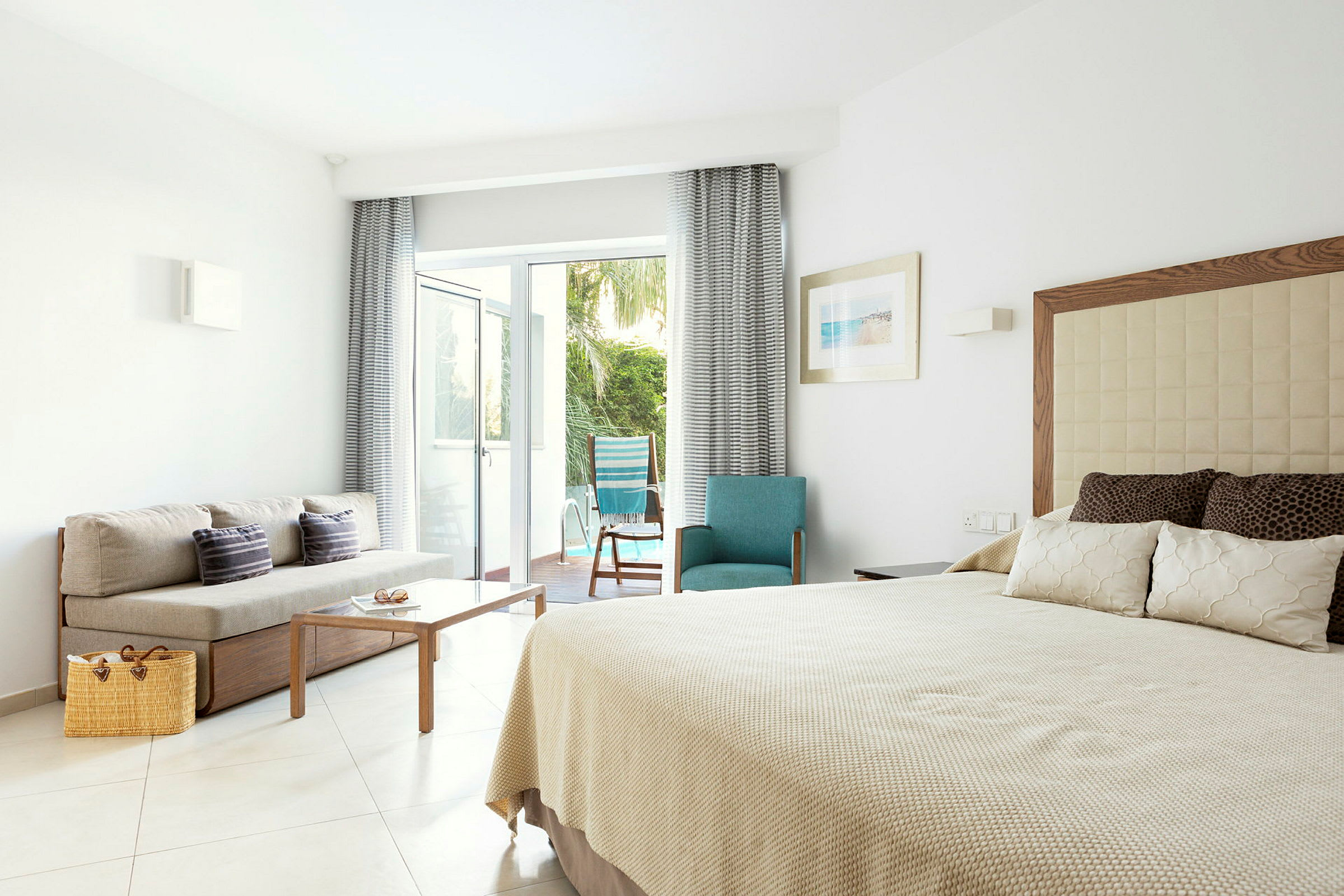 Hotellrum med säng, soffa och utsikt mot en uteplats med trädgård. (AI-genererad text)