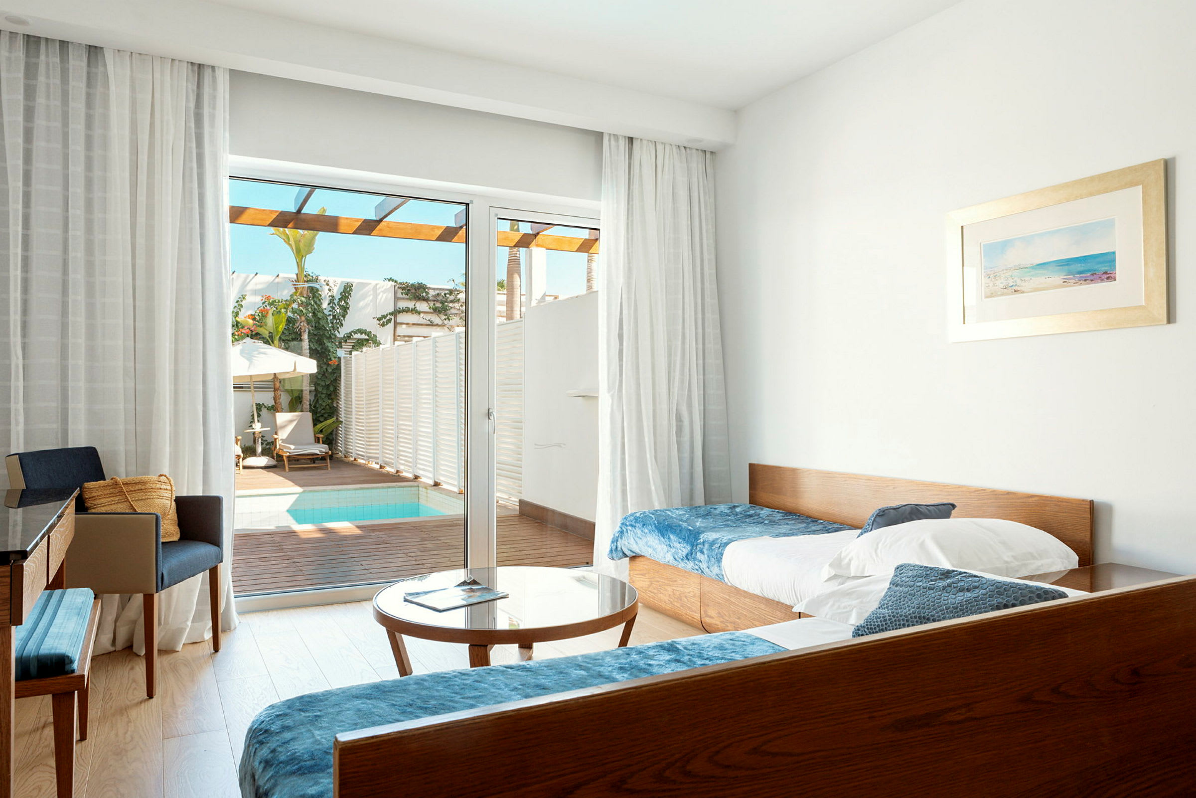 Ett hotellrum med sängar, bord och stolar, samt en glasdörr som vetter mot en terrass med liten pool. (AI-genererad text)