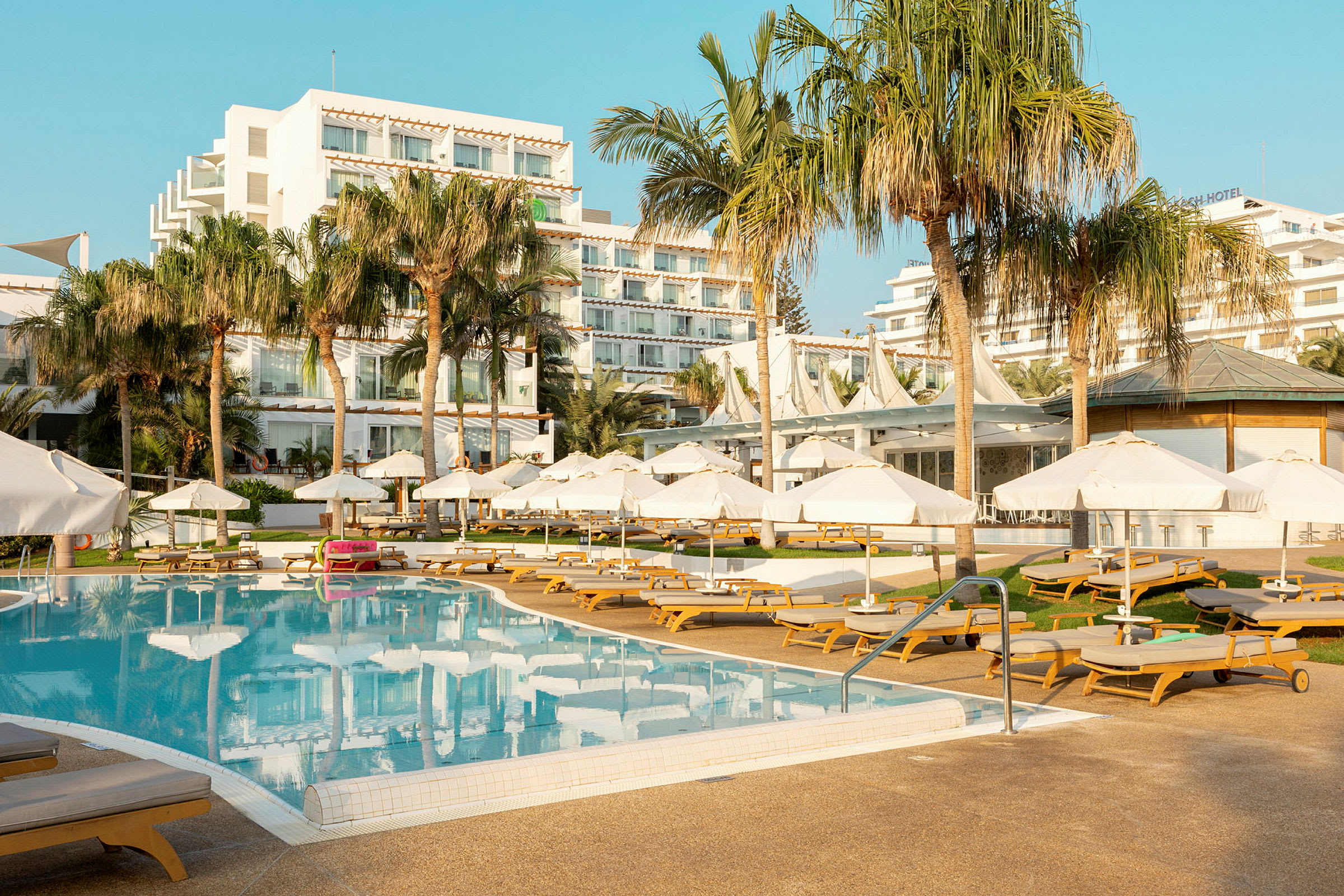 Bild av en hotellpool med solsängar och parasoller, omgiven av palmer och hotellbyggnader. (AI-genererad text)