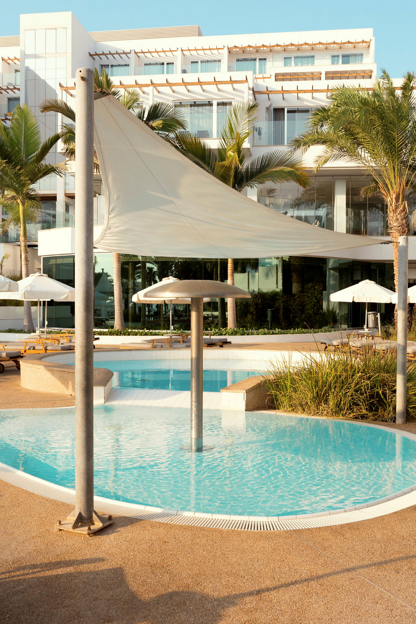 En hotellbyggnad med utsikt över en pool med solstolar och parasoller. (AI-genererad text)