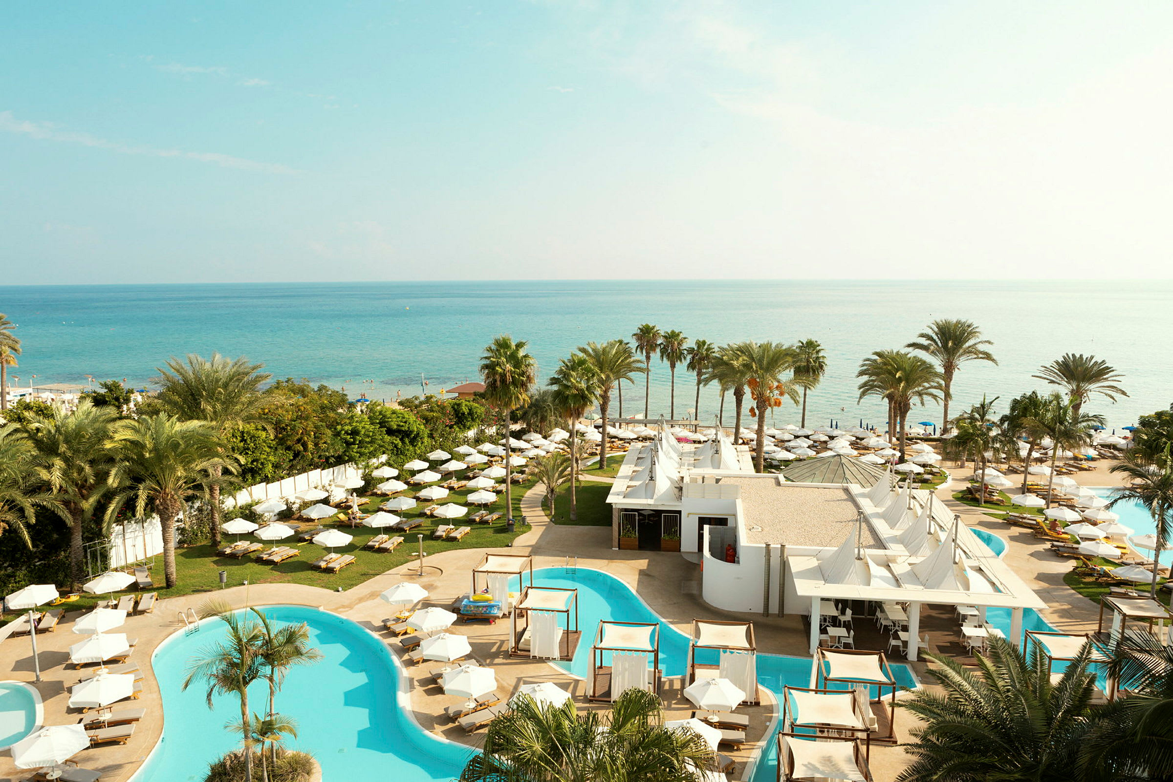 En hotellanläggning med pooler, solstolar och parasoller, och en utsikt över havet. (AI-genererad text)